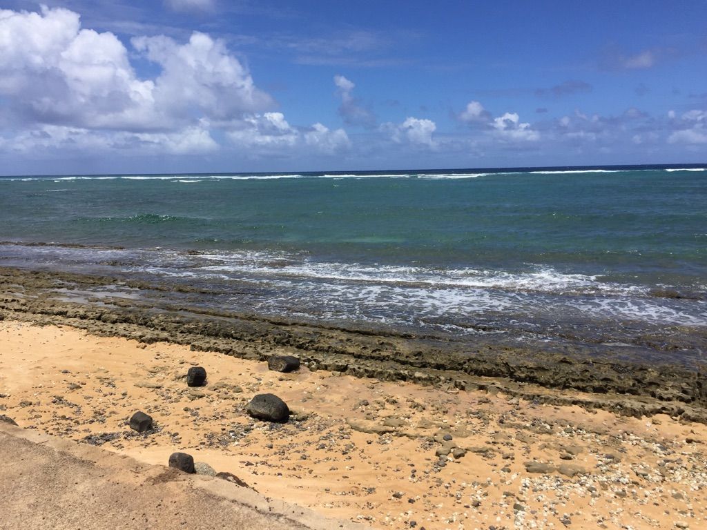 Sandy beach with scattered rocks and calm ocean under a blue sky. - Waipouli Beach – Waipouli Beach loop from Kapaa