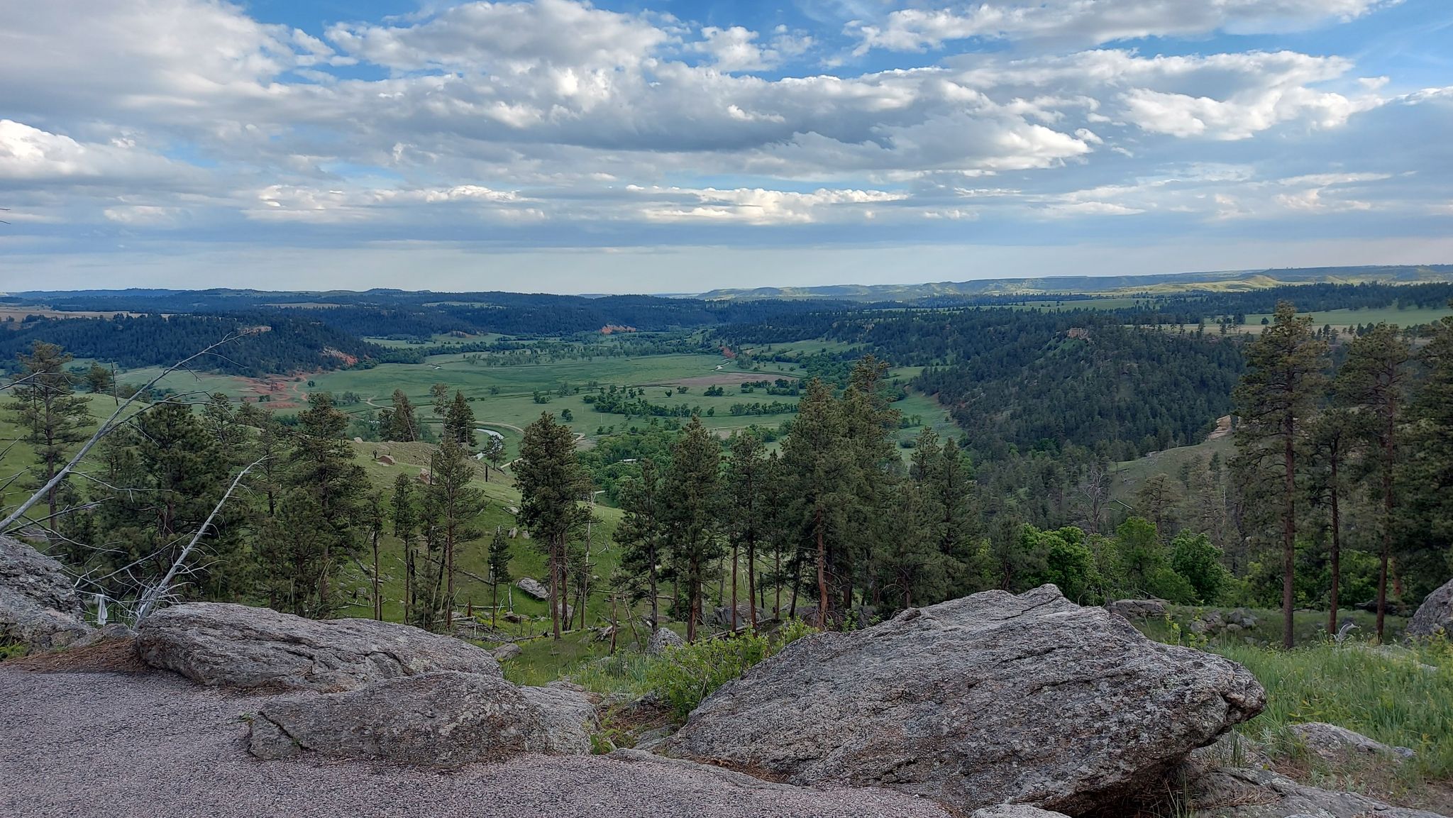 Panoramic view of a green valley and distant forested hills under a partly cloudy sky. - Tower Trail
