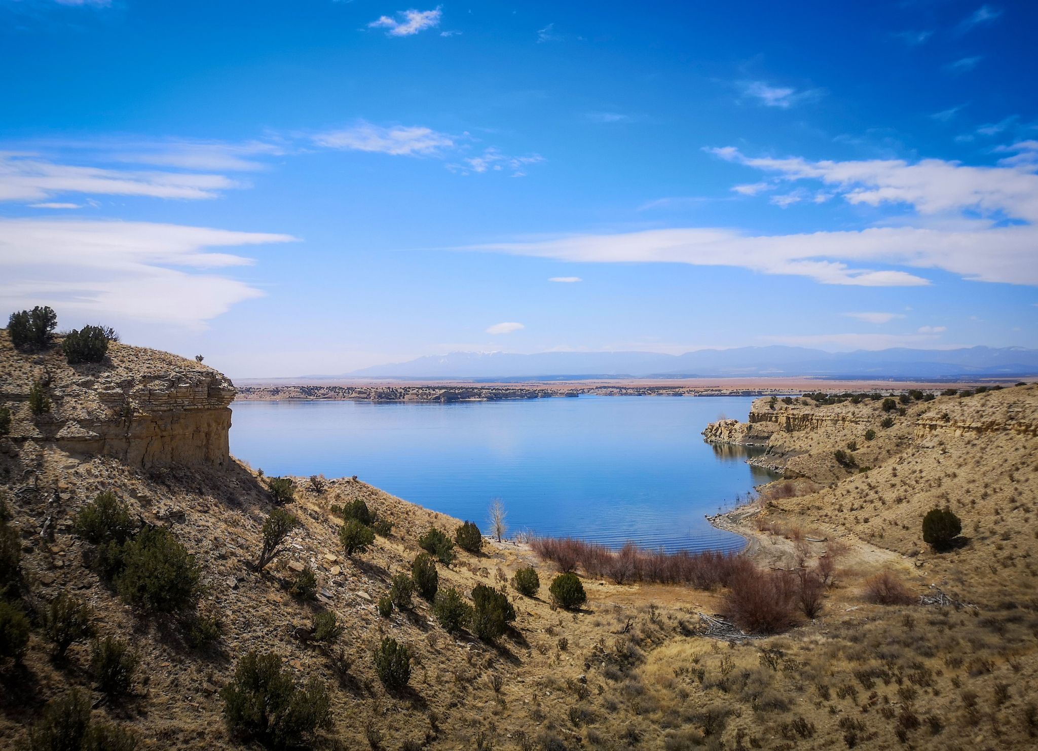 Vast blue lake nestled between arid rocky cliffs under a bright sky. - View of Pueblo Reservoir Dam – South Shore Trail Network loop from Pueblo West