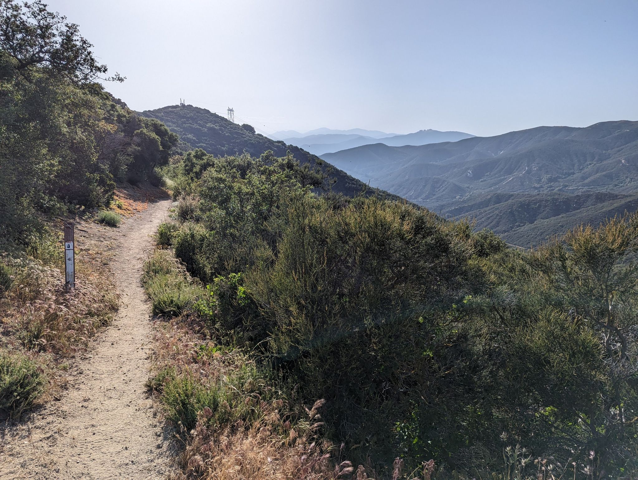Sunny dirt trail winding along a brush-covered mountain ridge with hazy mountains. - Pacific Crest Trail to Spunky Canyon