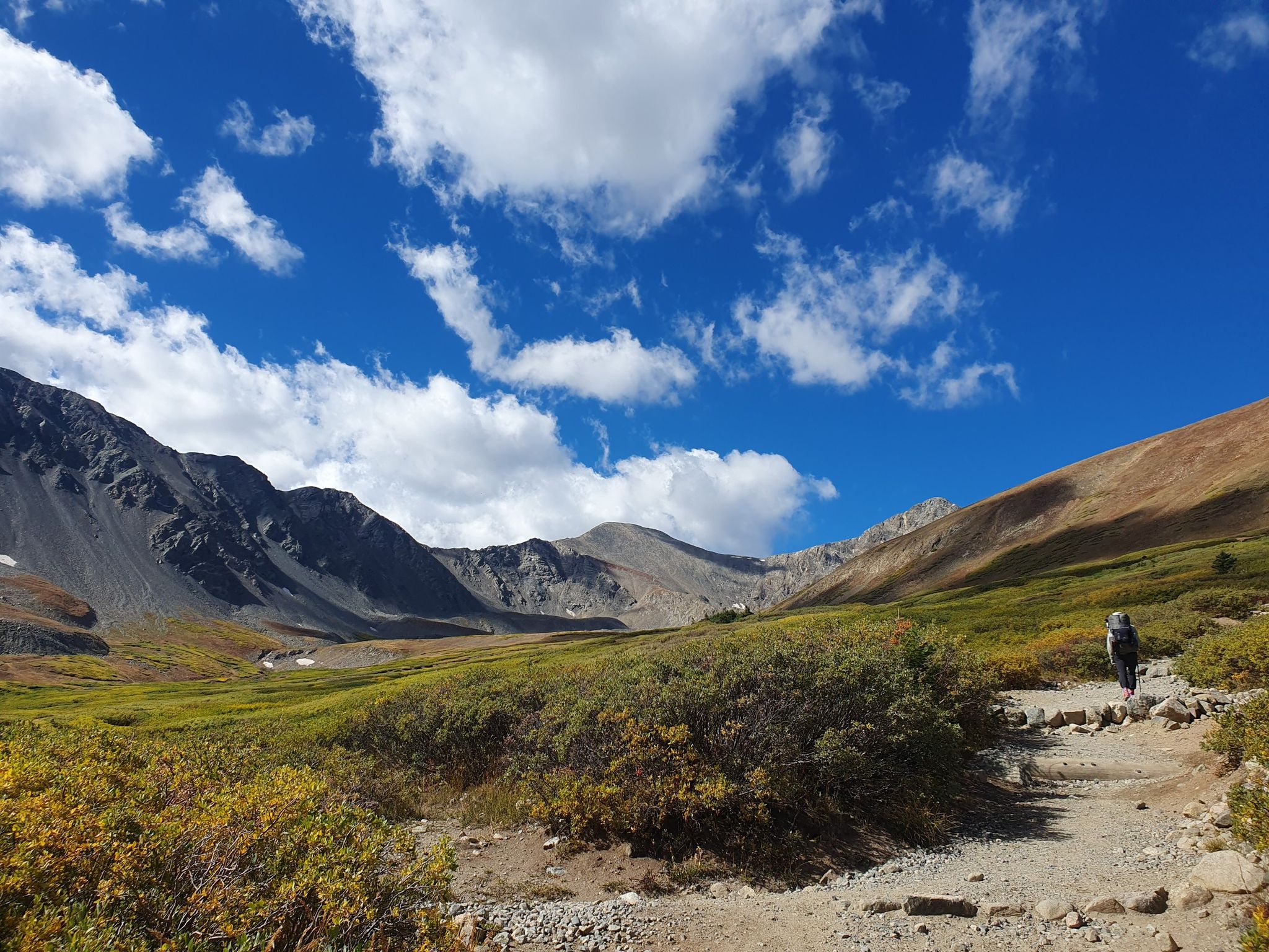 Hiker on a dirt path through a sunny mountain valley with clouds. - Grays and Torreys Peak Trail