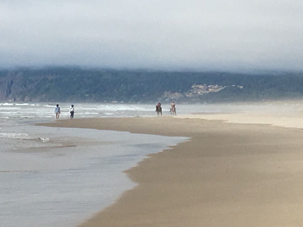 People and horses on a misty beach with ocean waves and distant cliffs. - Sunset and Nehalem Beach Walk