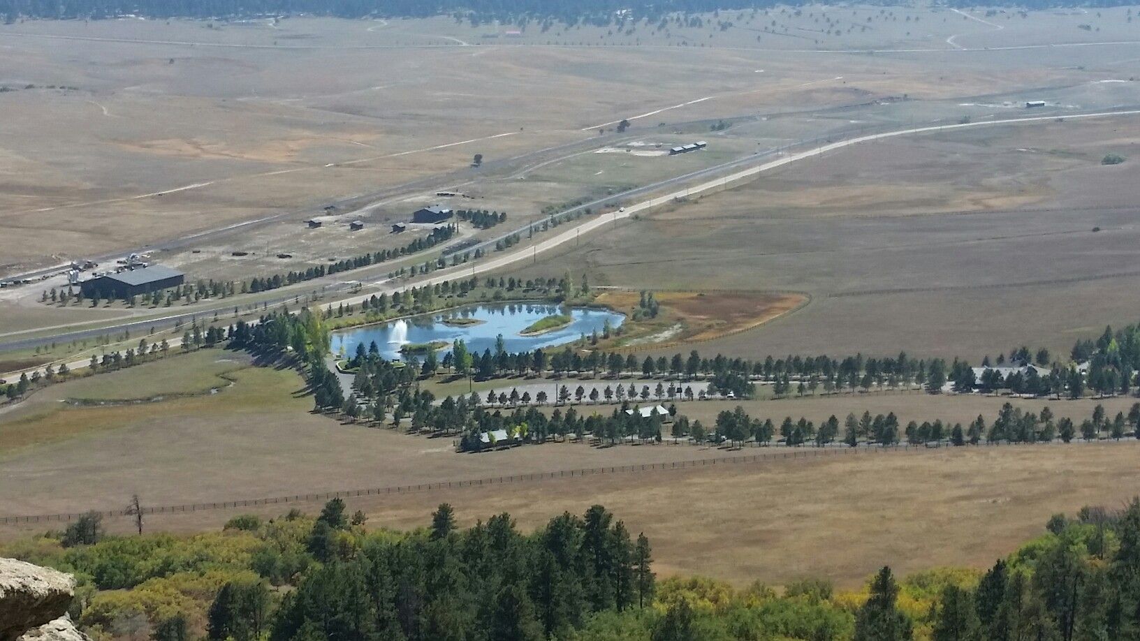 Aerial view of a road, pond, and buildings in a vast, open landscape. - Spruce Mountain Trail Loop