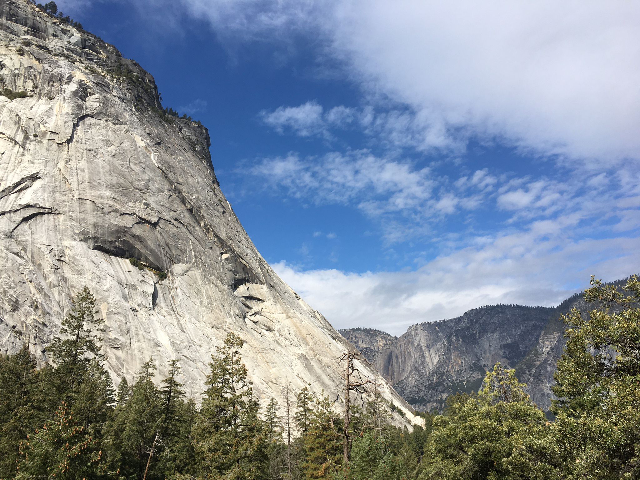 A massive, textured granite cliff face under a bright blue sky. - Mist Trail to Vernal Fall