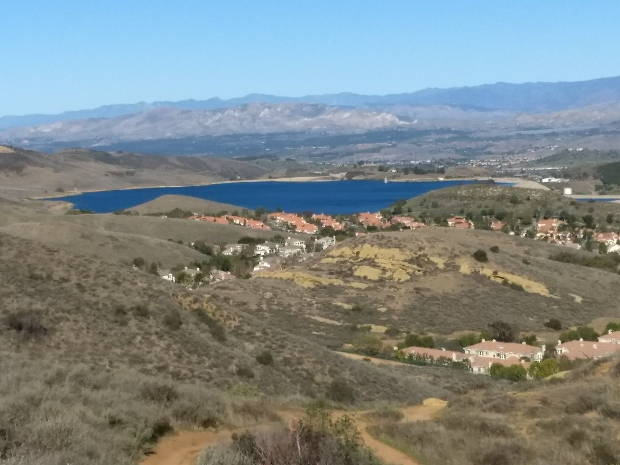 Panoramic view of a blue lake, houses, and distant mountains. - Hiking loop from Bard Lake