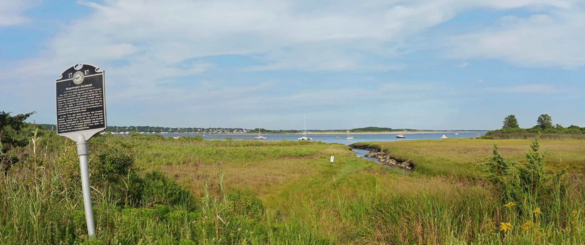 An informational sign in a grassy field overlooking a bay with boats. - Seapowet Marsh Management Area – Acoaxat Beach loop from Dartmouth