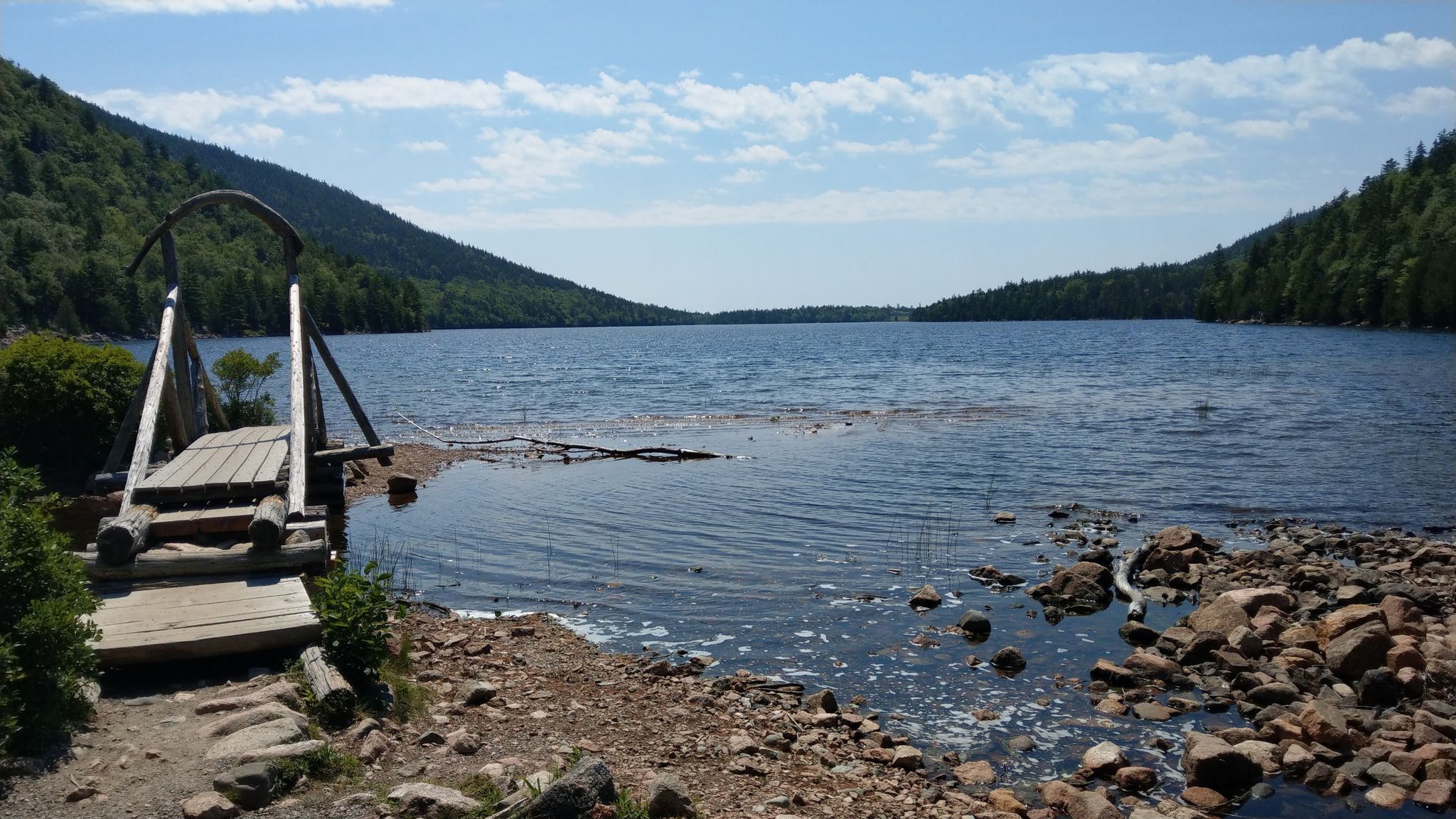 Sunny day, wooden bridge leading to a rocky lake shore with forested hills. - Jordan Pond Path and South Bubble Trail