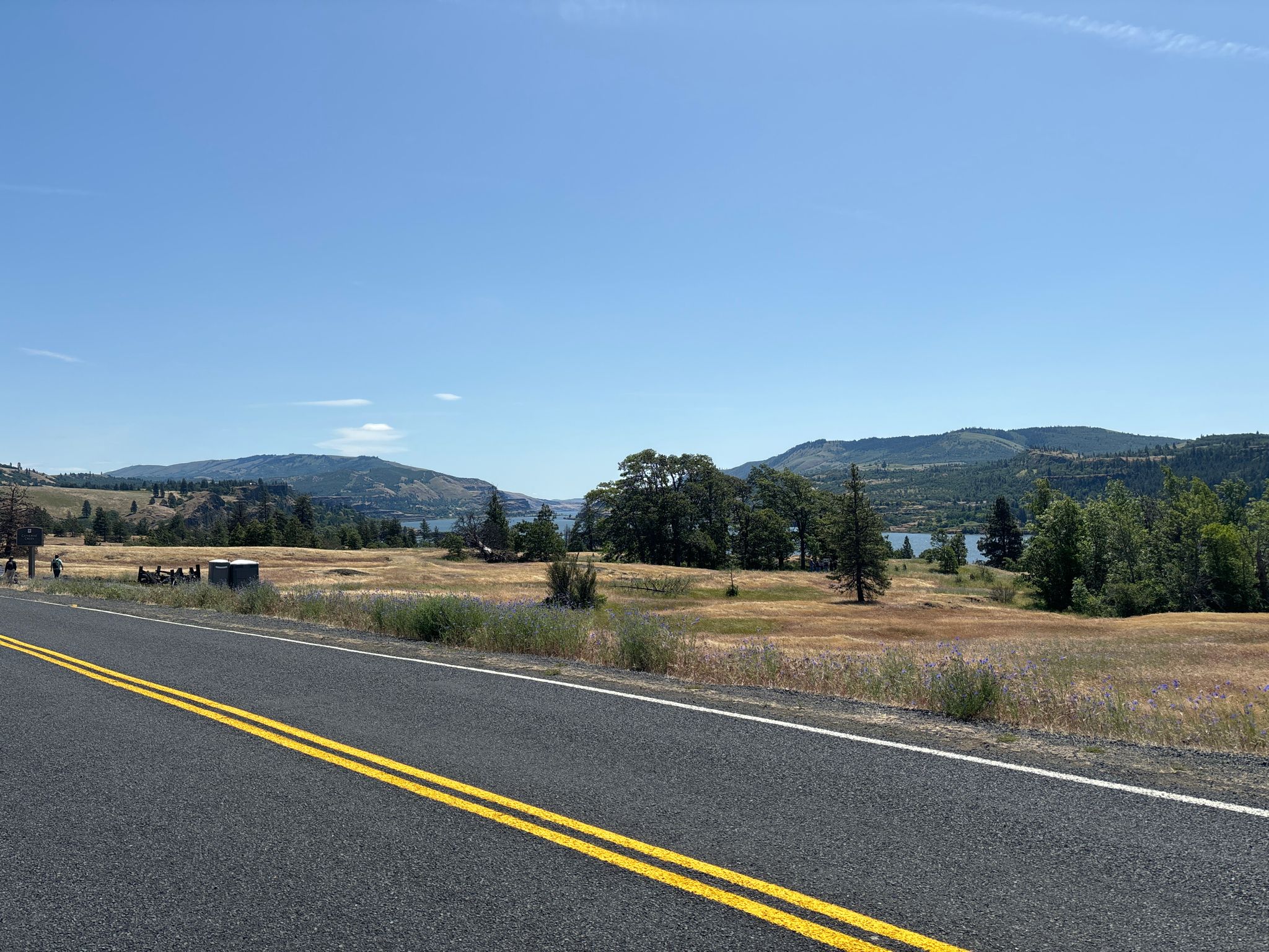 Roadside view of dry fields, scattered trees, and distant water under blue sky. - Catherine Creek Arch Loop
