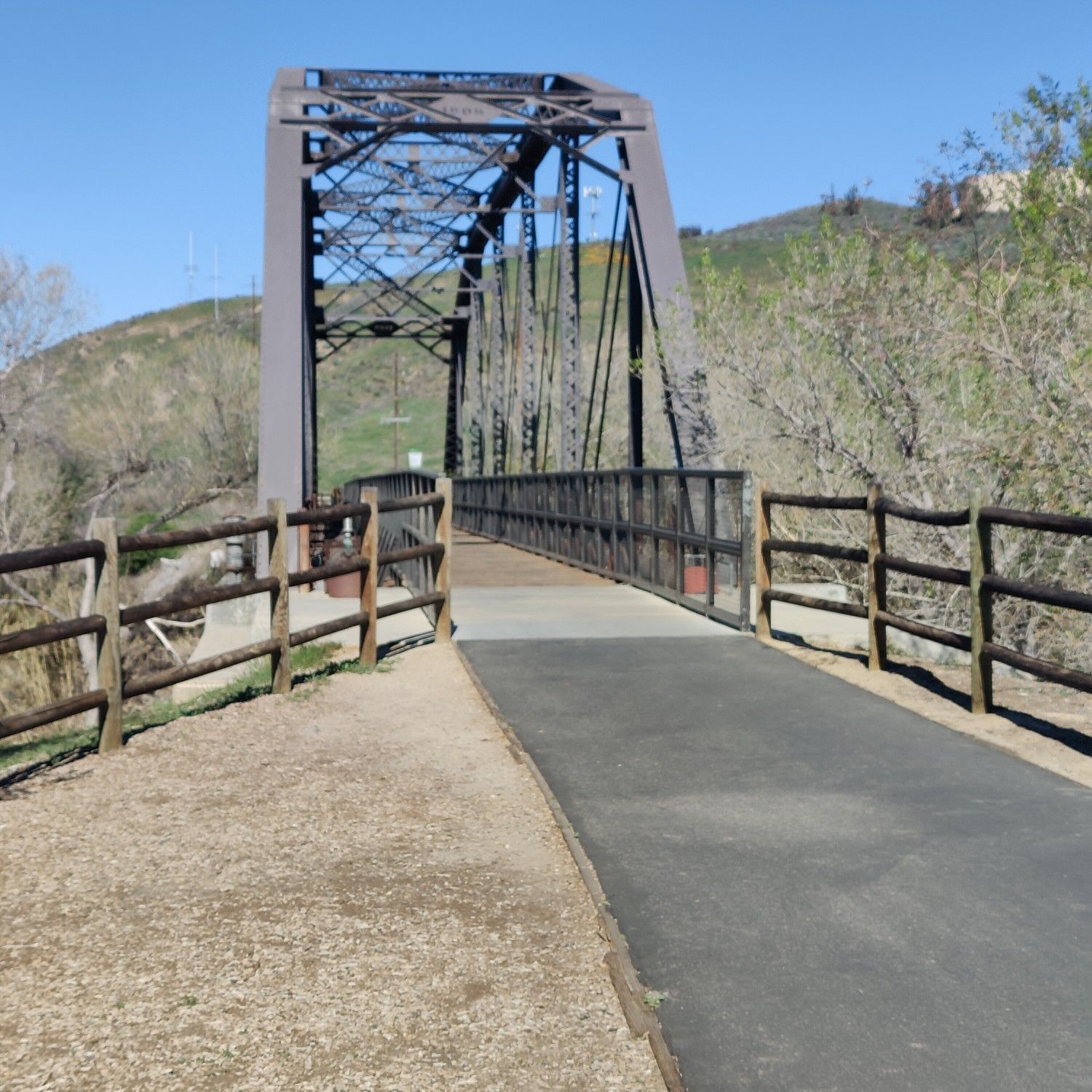 A paved path leads to a large metal truss bridge over a dry landscape. - San Francisquito Creek Trail Loop