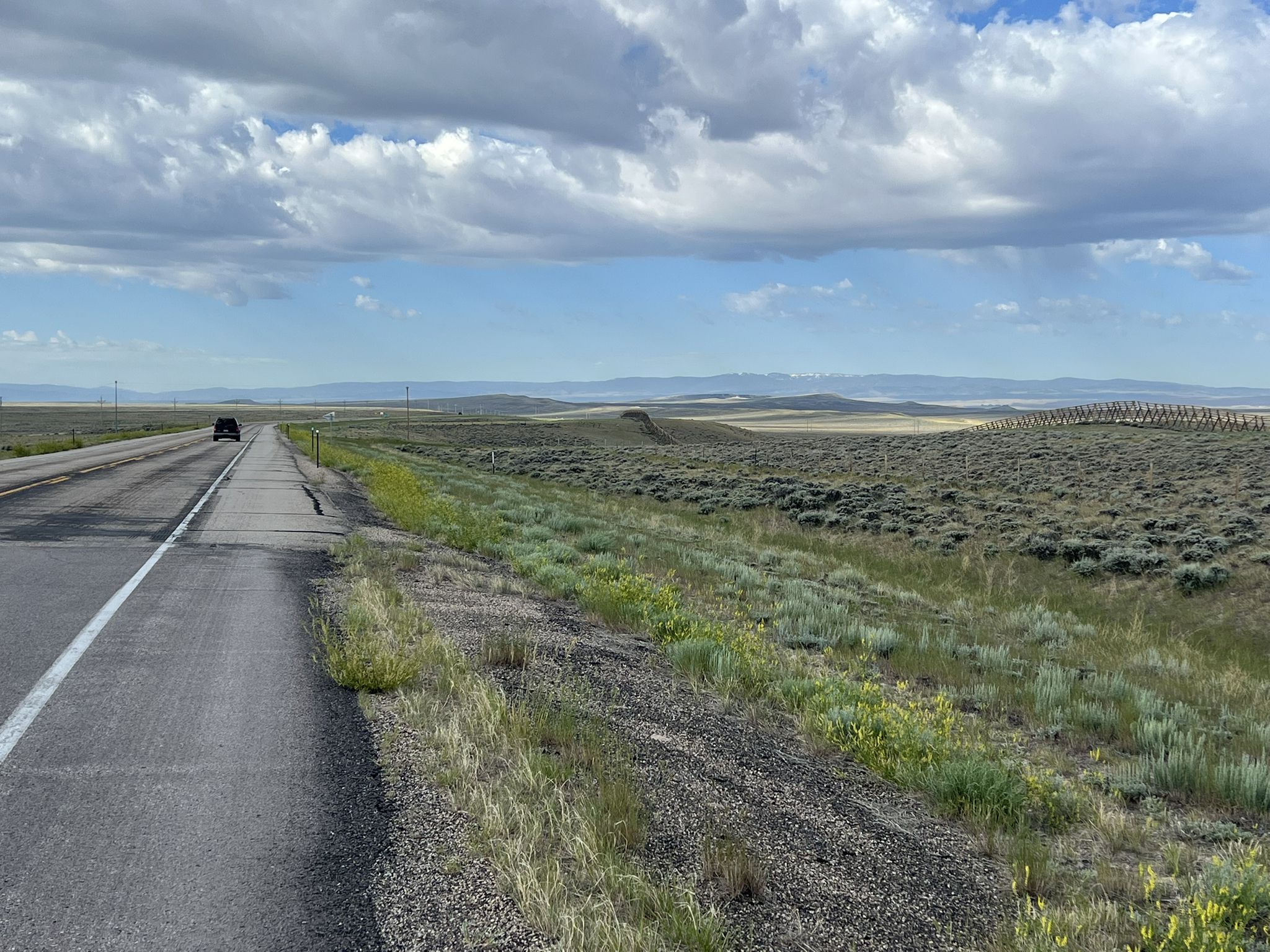 A long road stretches through arid plains under a cloudy sky. - TransAmerica Trail: Rawlins to Saratoga