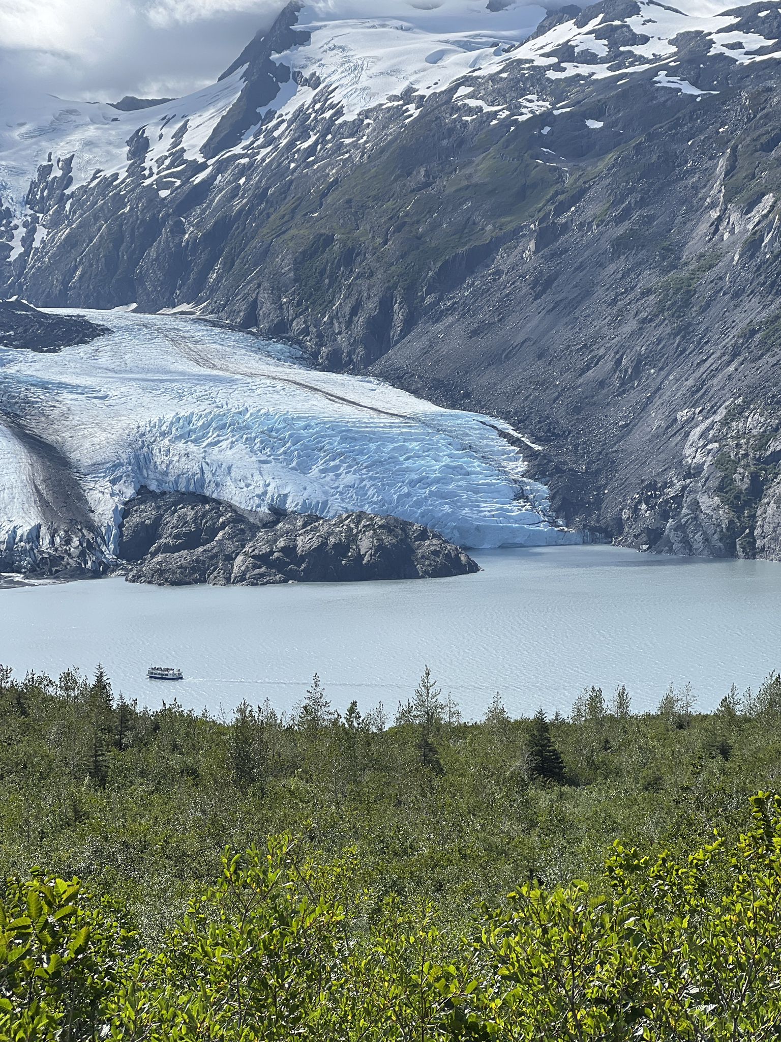 Large blue glacier descends into a calm lake with a boat, surrounded by mountains. - Portage Pass – Shoreline of Portage Lake loop from Whittier Airport