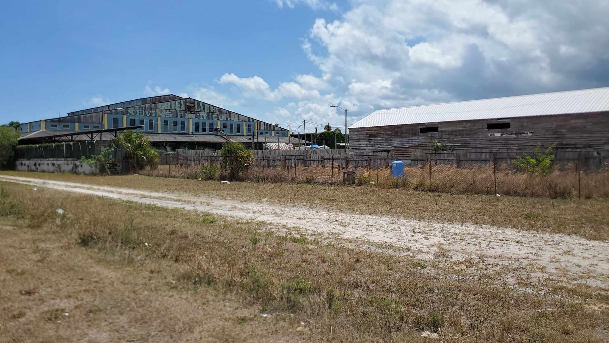 Two large industrial-style buildings behind a fence in a dry, grassy field. - East Central Regional Rail Trail Loop