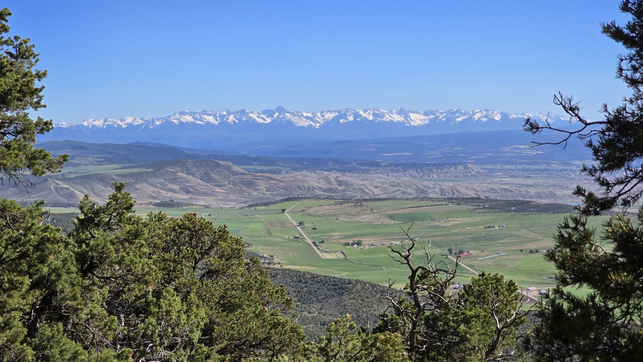 Green valleys and fields stretch towards distant snow-capped mountains under a clear sky. - Warner Point Nature Trail