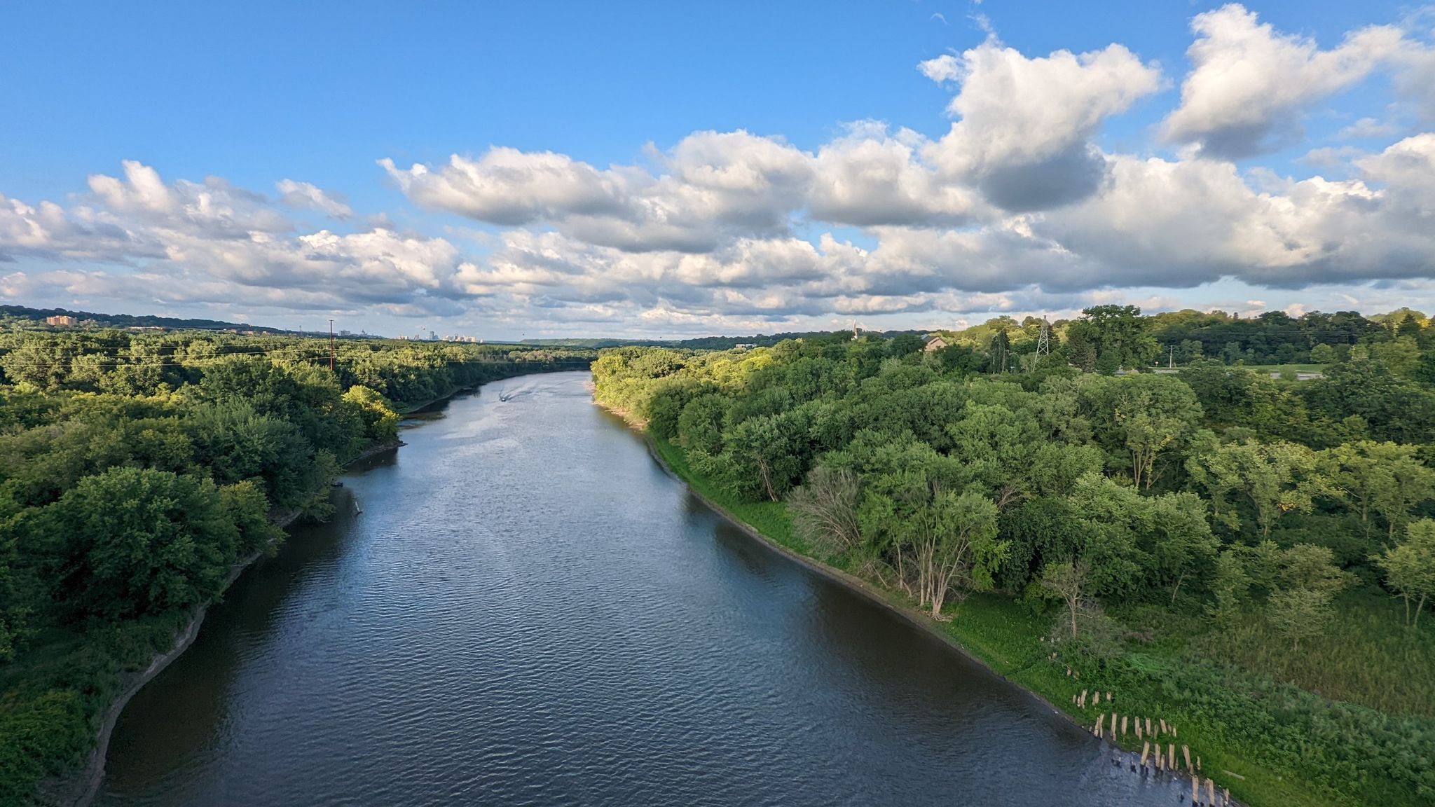 Wide river flowing through a lush green forest under a cloudy blue sky. - Snelling Lake, Fort Snelling, Picnic Island Loop