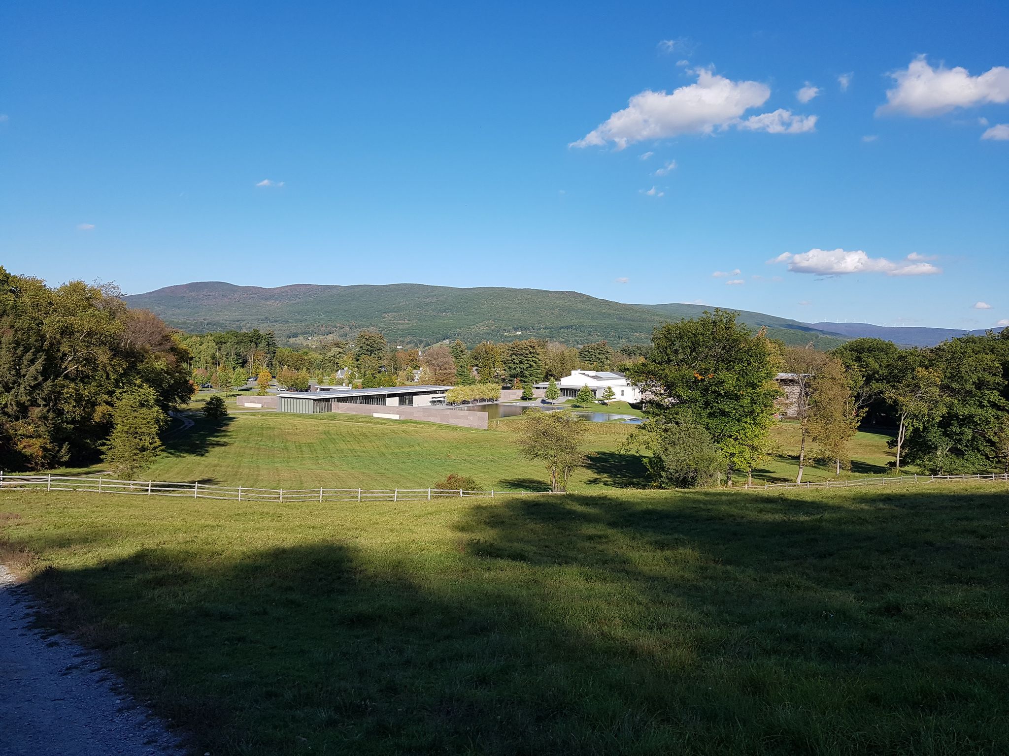 Sunny view of green fields, distant buildings, and mountains under a clear blue sky. - Fitch Memorial Lands – Stone Bench Trail loop from Mount Greylock Regional School