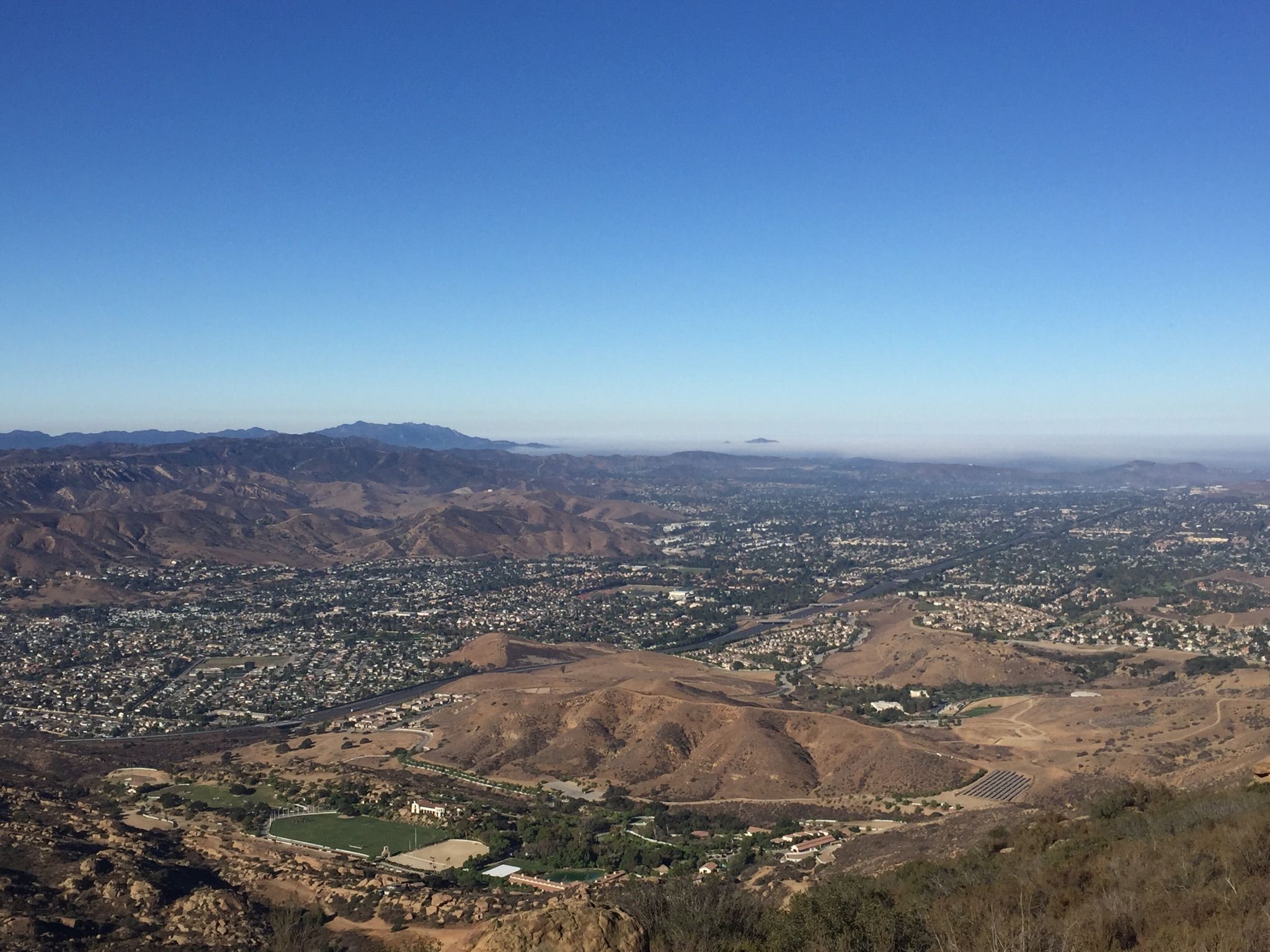 Panoramic view of a sprawling city in a valley, surrounded by distant mountains. - Santa Susana Pass Road – Santa Susana Pass (Simi Pass) loop from Simi Valley