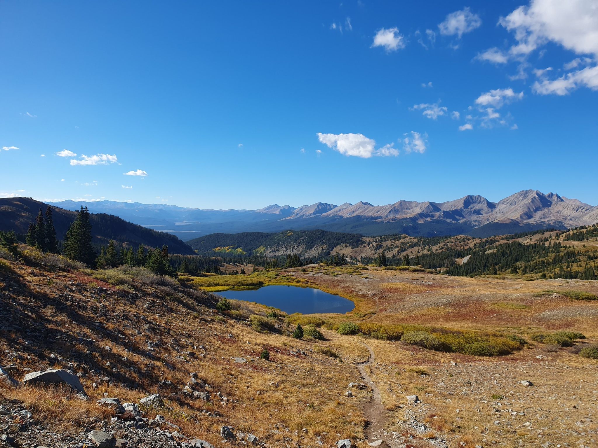 Sunny alpine landscape with a small lake, distant mountains, and a winding trail. - Cottonwood Pass – View of Cow Lake loop from Continental Divide