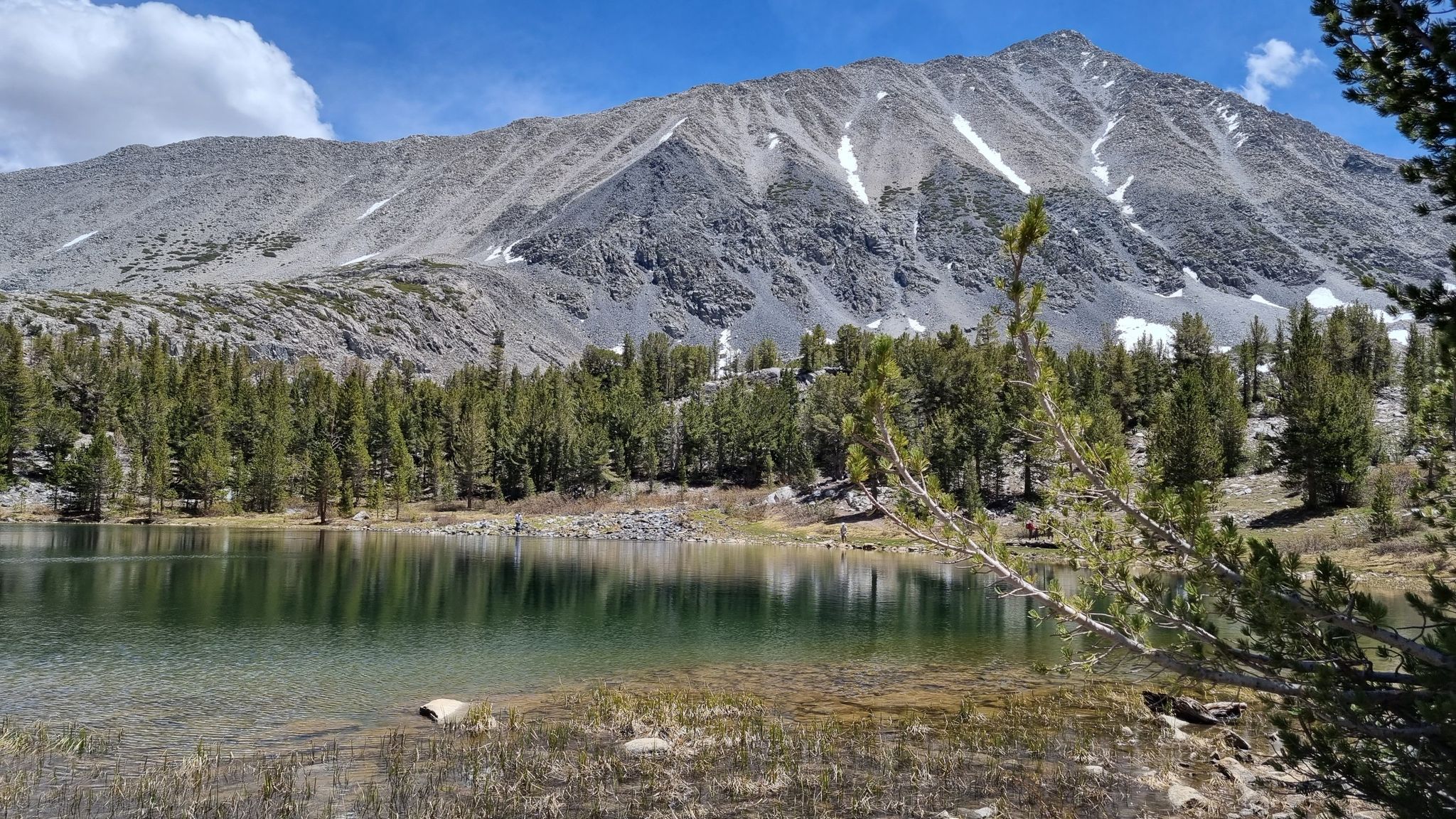 A clear lake reflects a large, rocky mountain with patches of snow. - Little Lakes Valley Trail
