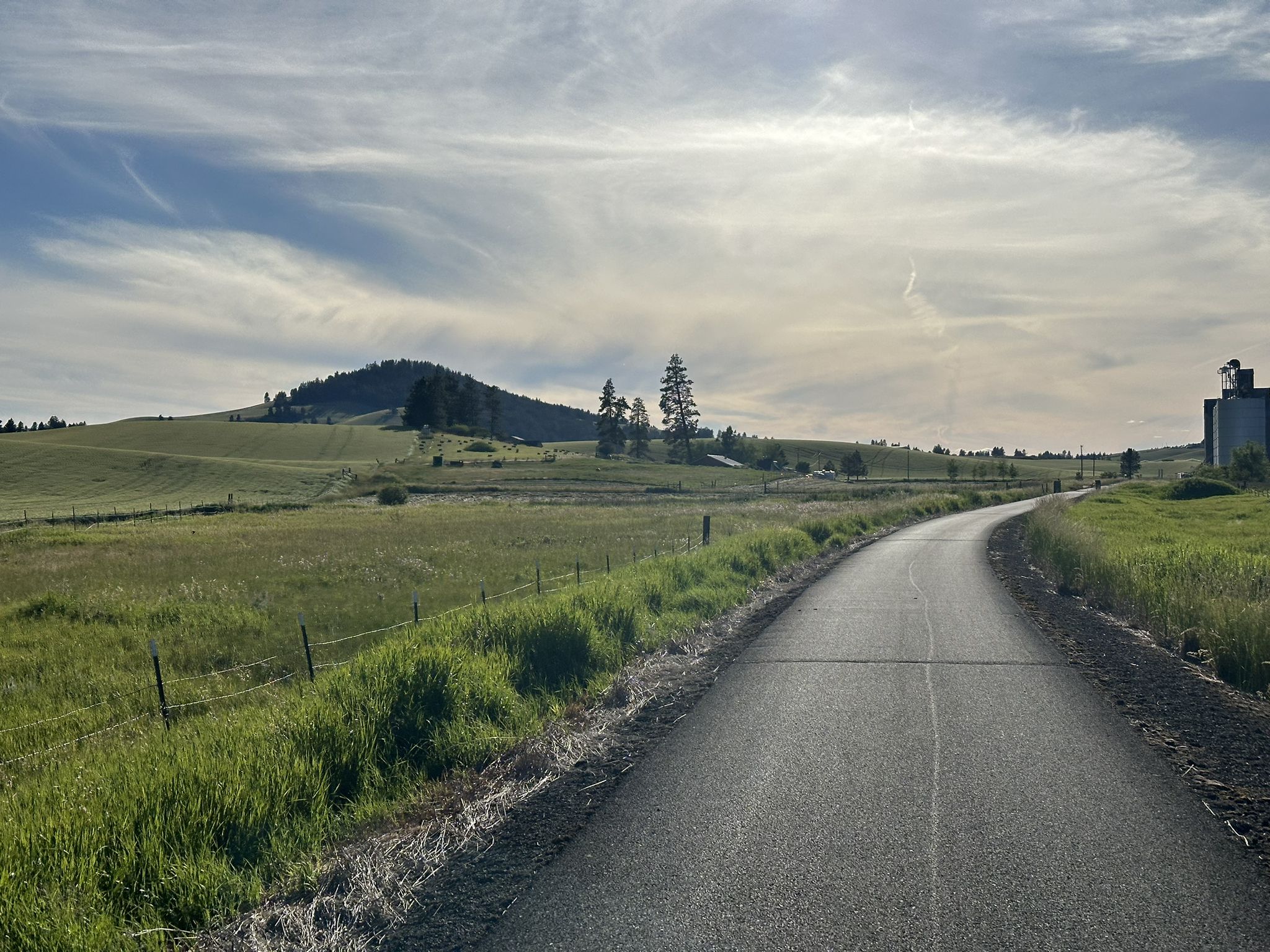 Paved road winding through green fields towards a distant hill under a cloudy sky. - Paradise Path – Stone Wall Bench loop from Moscow