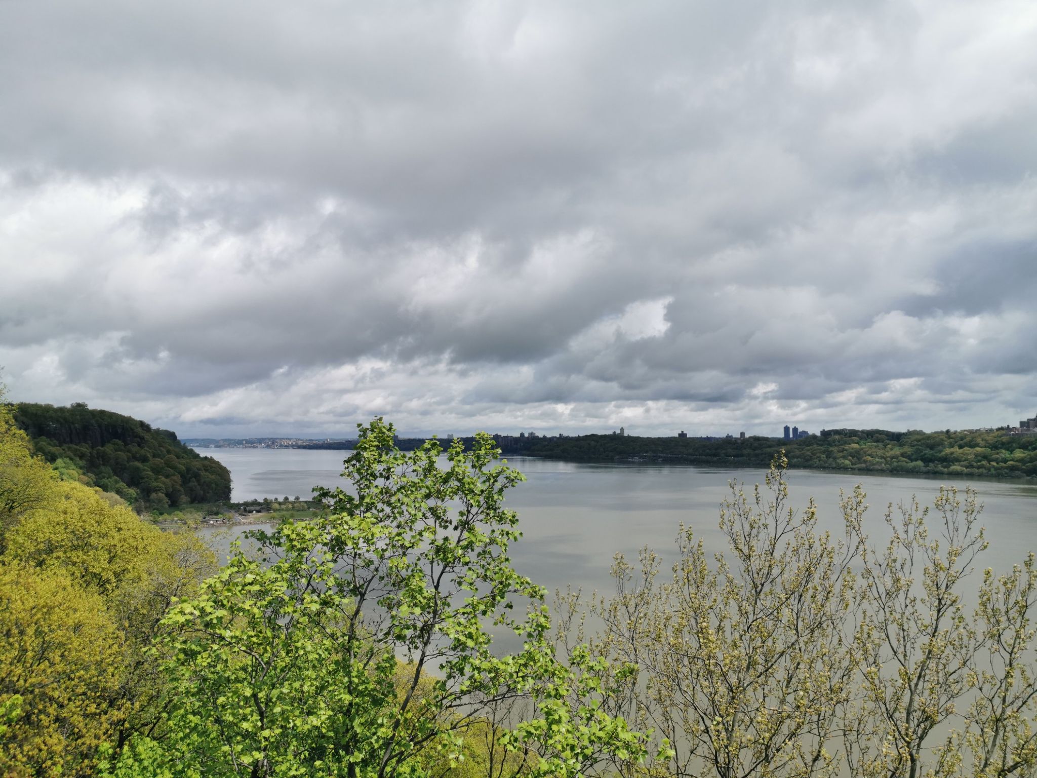 Wide river seen from a forested viewpoint under a dramatic, cloudy sky. - The Little Red Lighthouse – Climb up to Alpine loop from Dyckman Street