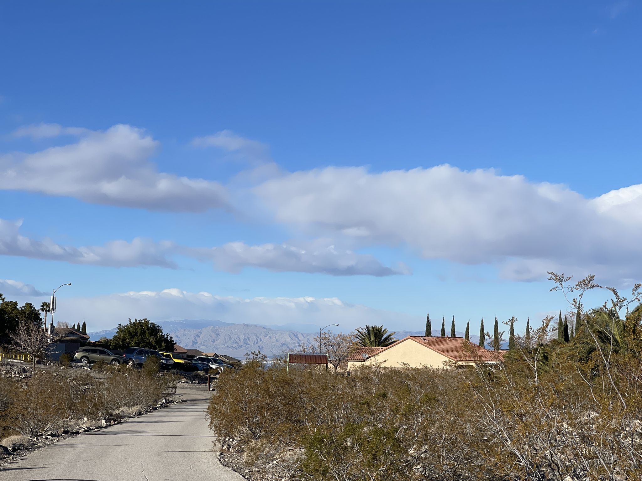A desert road leads towards houses and distant mountains under a cloudy sky. - 403 Trail and Park Peak Loop