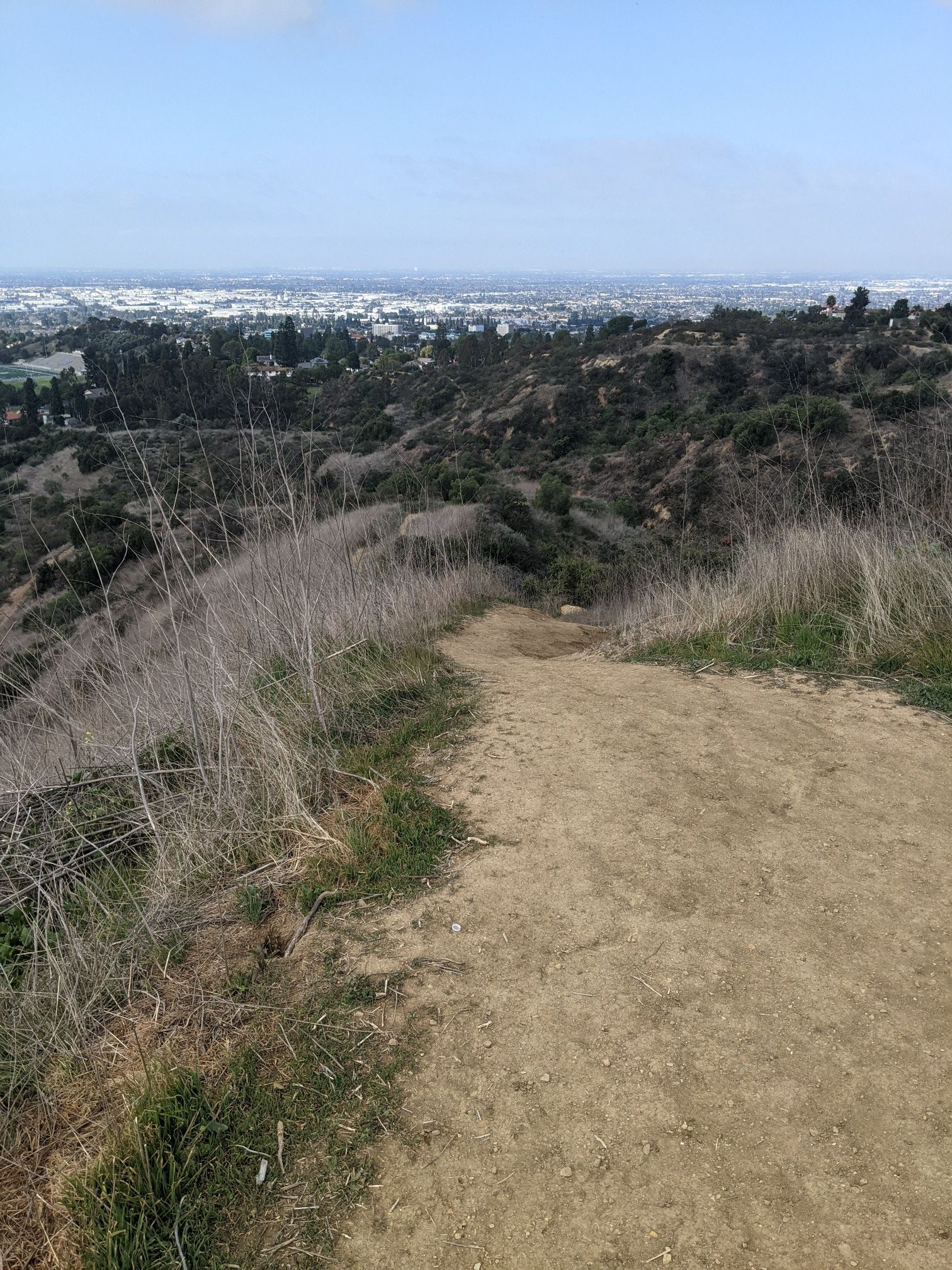 A dirt path descends through dry grass with a city visible beyond. - Workman Ridge and Worsham Canyon Trail