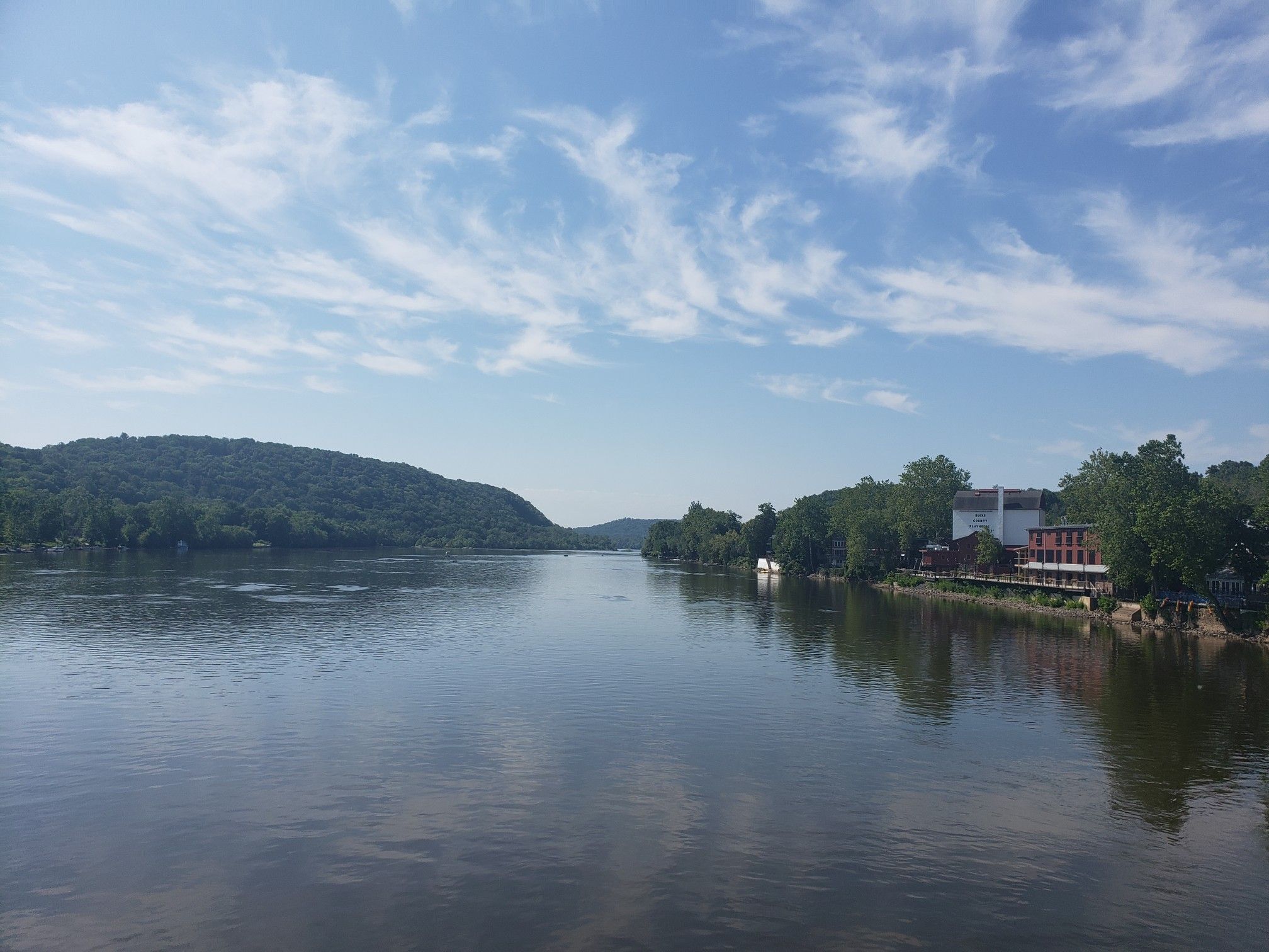 A wide river reflects a bright sky with scattered clouds and green hills. - New Hope Loop