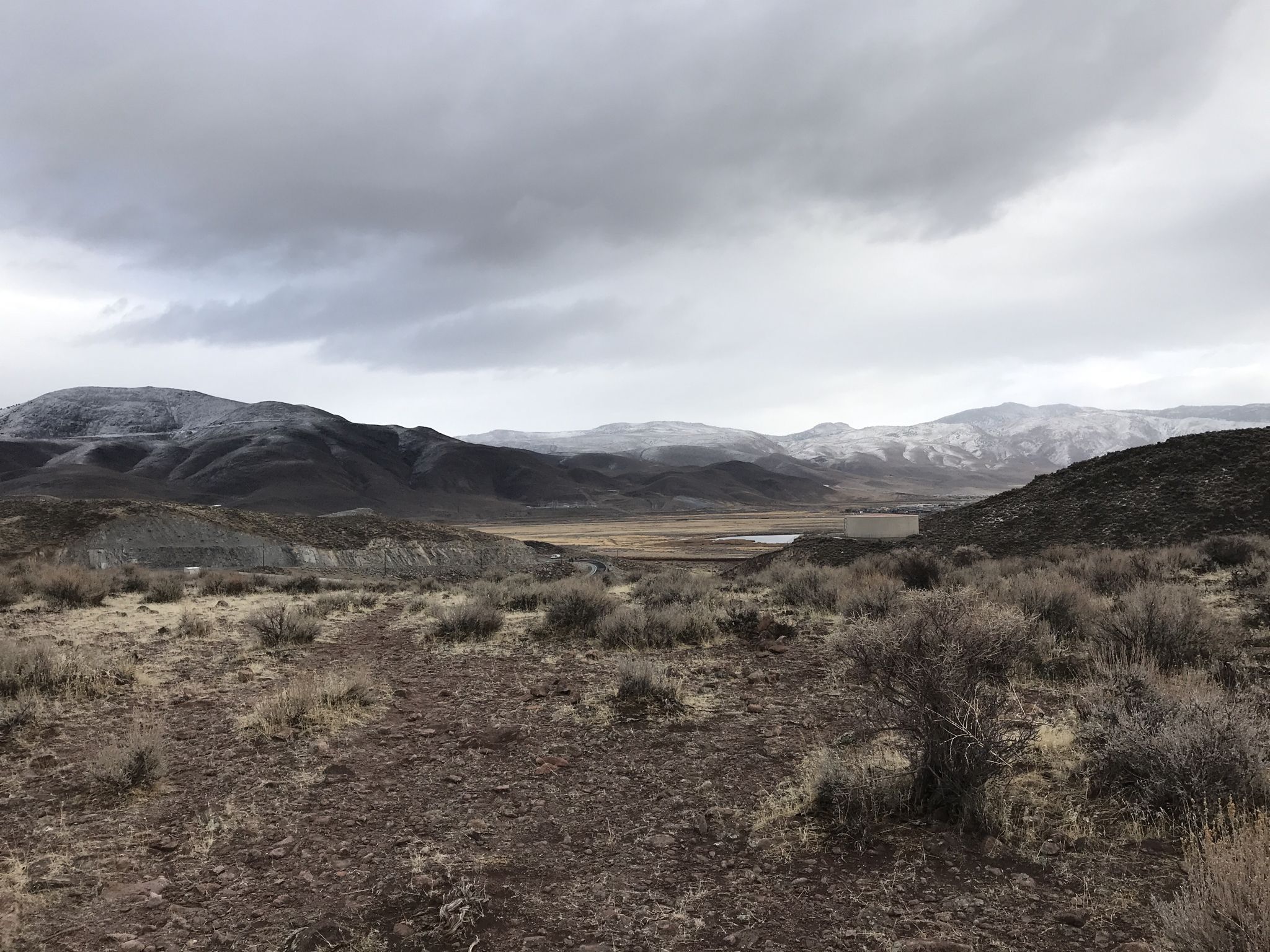 Expansive arid landscape with rolling hills and distant snow-dusted mountains under cloudy skies. - Huffaker Hills Peak
