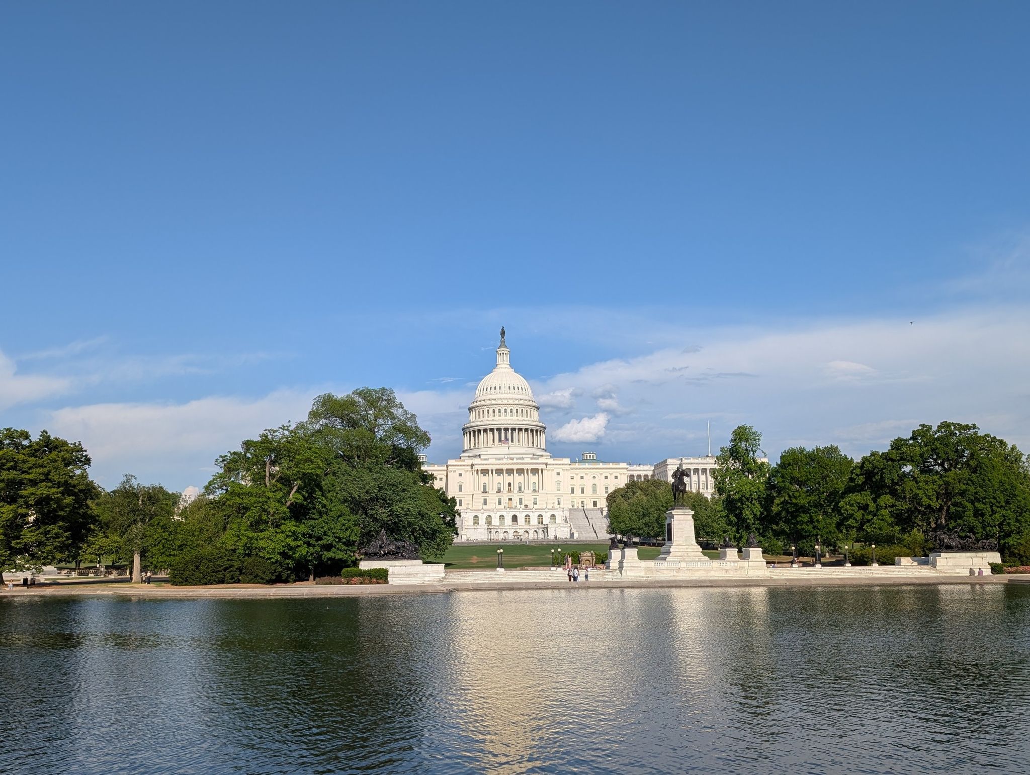 Domed building behind water, green trees, clear blue sky. - U.S. Capitol – Washington Monument loop from NoMa–Gallaudet U
