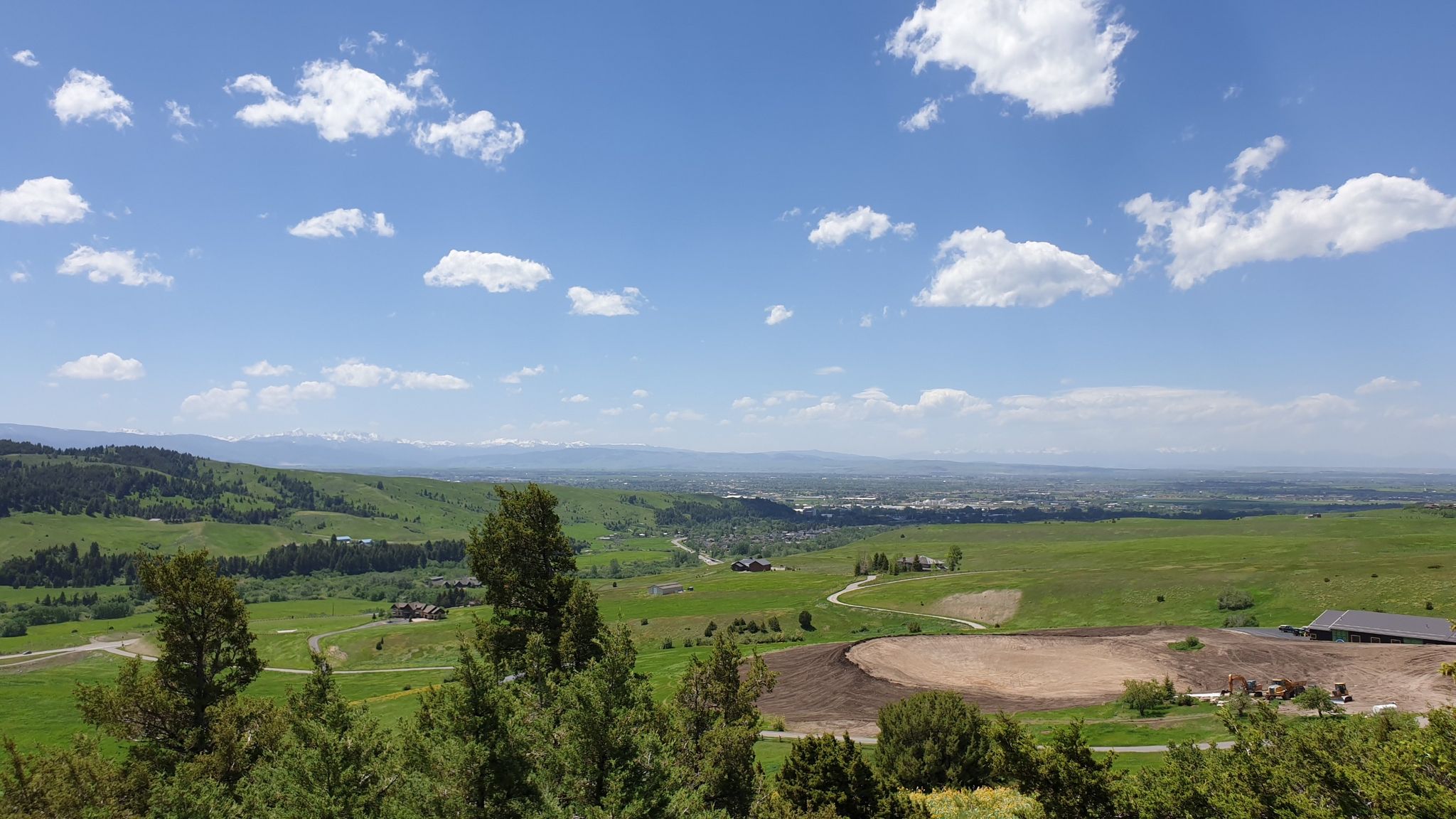 Expansive view of green rolling hills, distant city, and blue sky with clouds. - College M and Bridger Foothills Trail