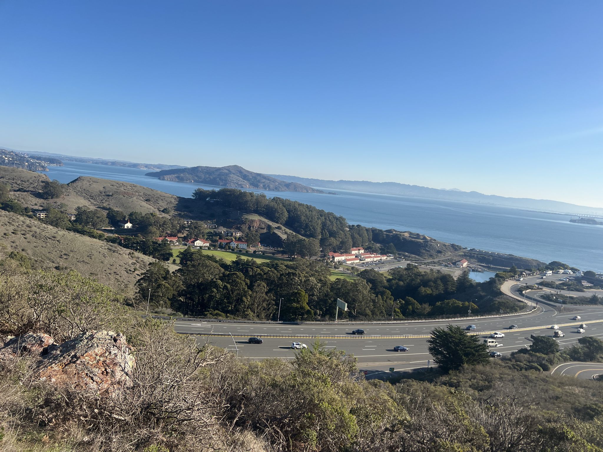 Sunny view of coastal hills, busy highway, blue bay, and distant island. - Slacker Hill via SCA Trail