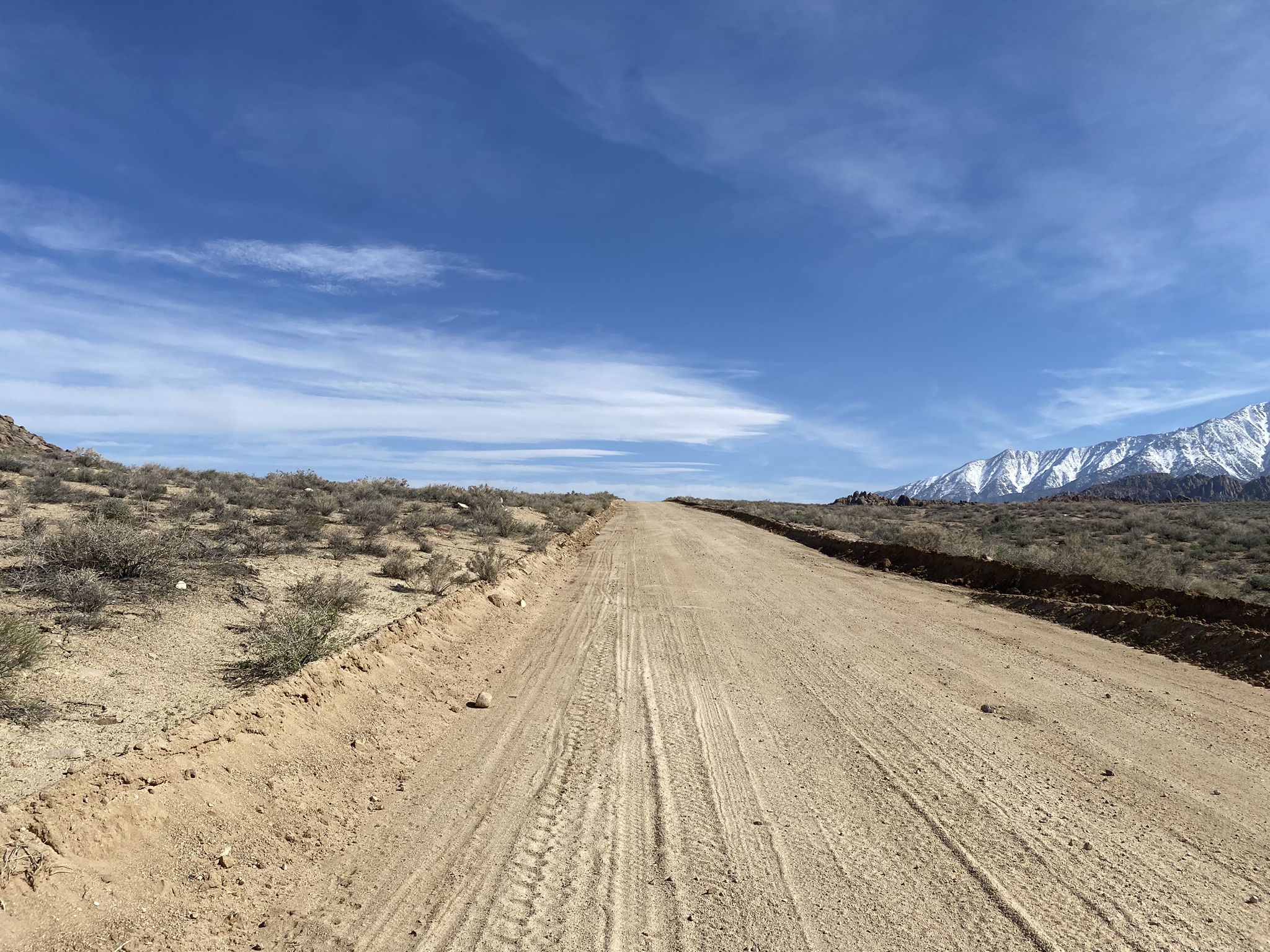 A dirt road leads towards snow-capped mountains under a bright blue sky. - Alabama Hills loop — Gravel