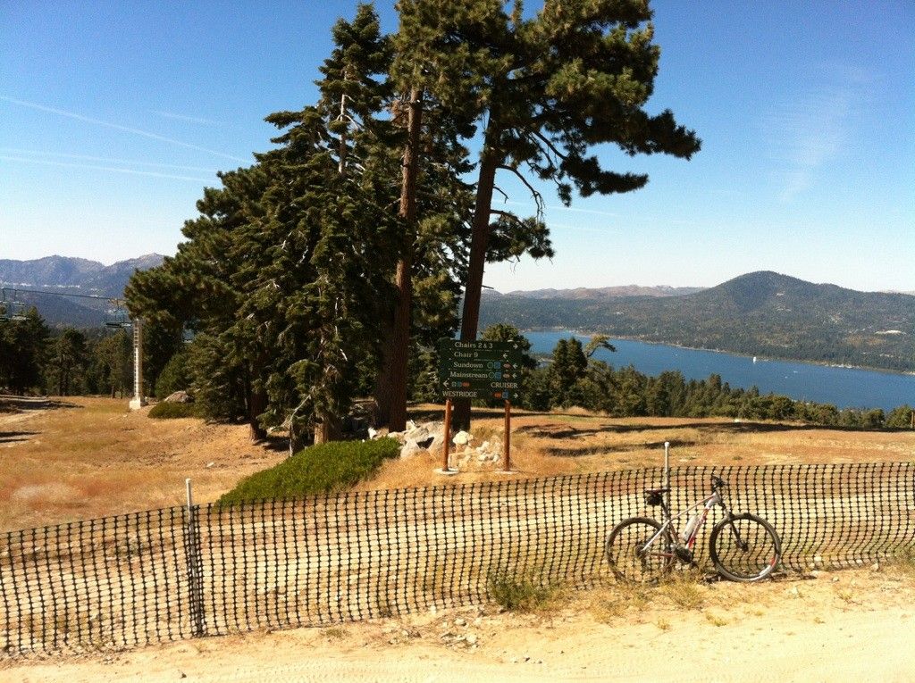 A mountain bike rests by a fence, overlooking a lake and distant mountains. - Snow Summit Parking Lot loop from Chair 1 East-Mountain Xpress