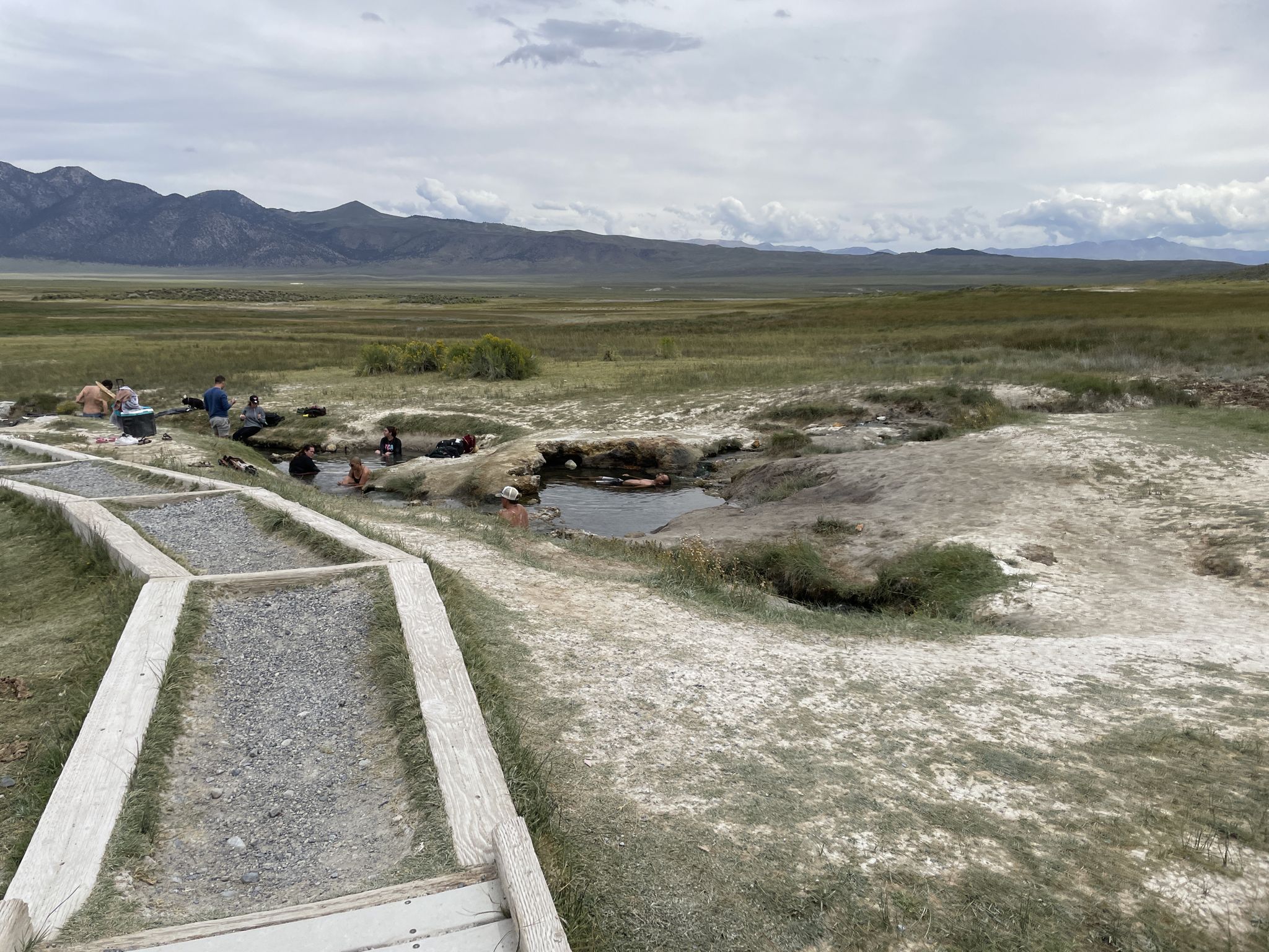 People soaking in natural hot springs beside a boardwalk, with distant mountains. - Mammoth Lakes, California to Wild Willie Hot Springs