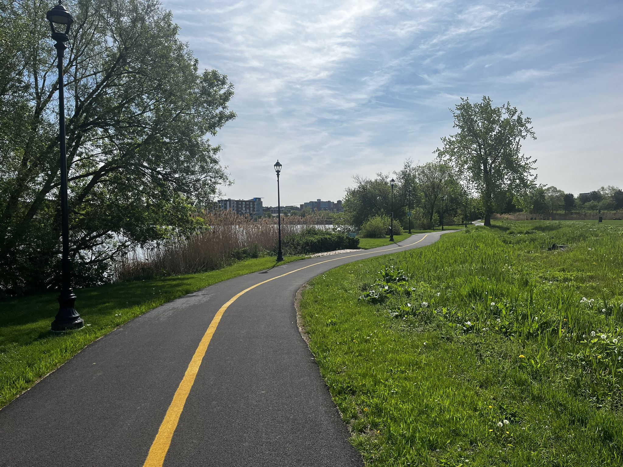 Paved path with yellow line curves beside water and green grass on a sunny day. - Niagara Hudson Building loop from Syracuse