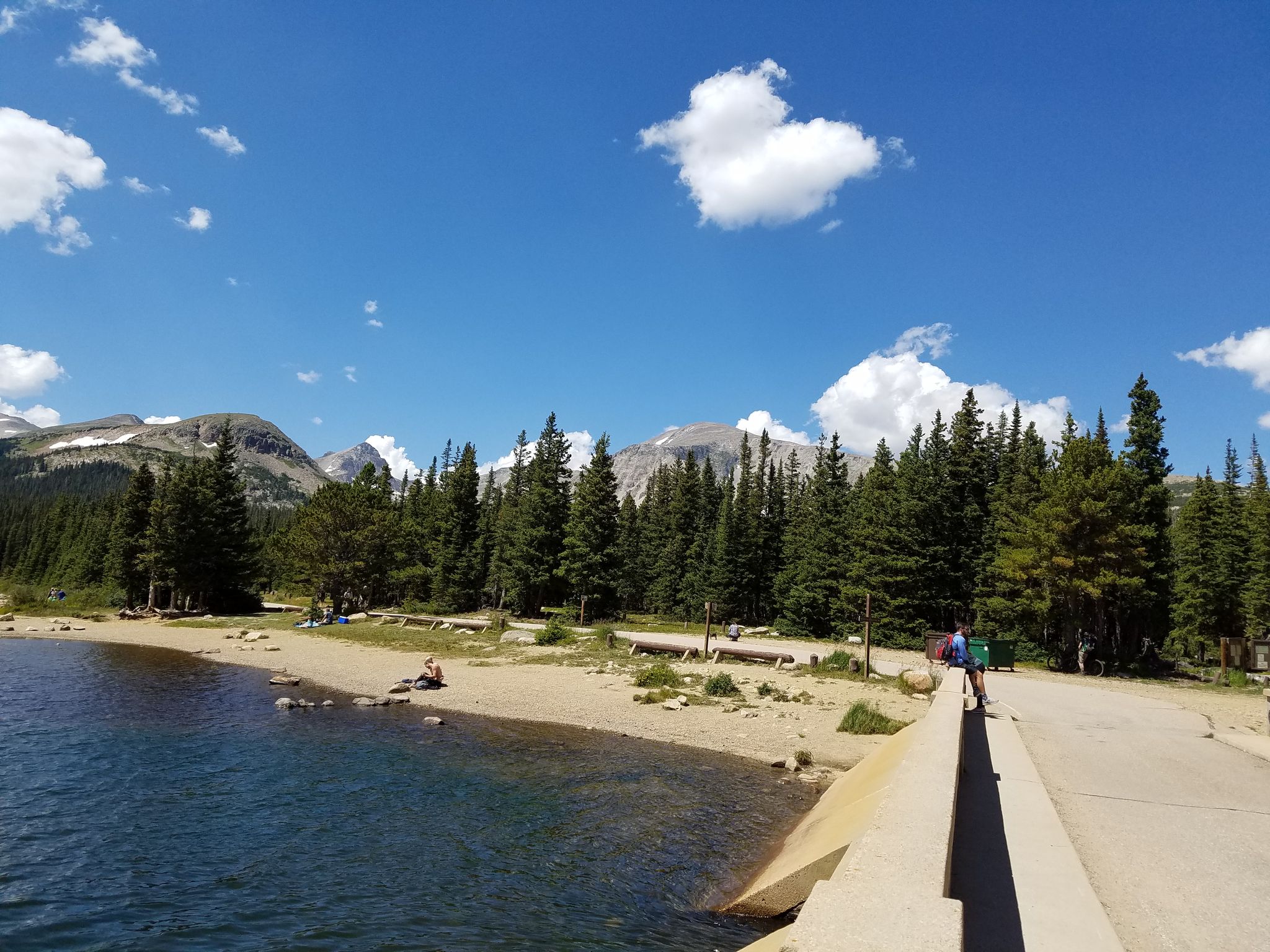 Sunny day at a lake with sandy shore, pine trees, and distant mountains. - Ward and Brainard Lake via Lee Hill Drive from Pearl Street