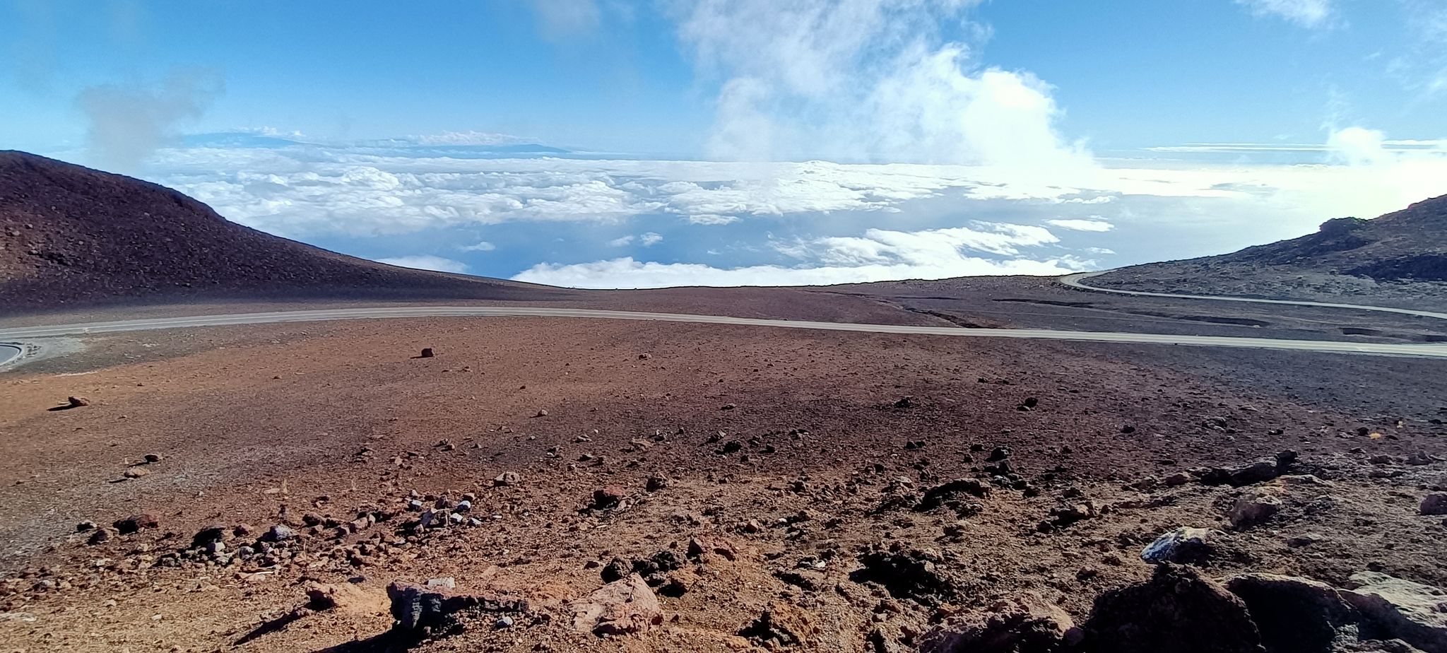 Barren, rocky landscape with a winding road and clouds below a blue sky. - Haleakalā Visitor Center – Summit Building loop from Pan-STARRS