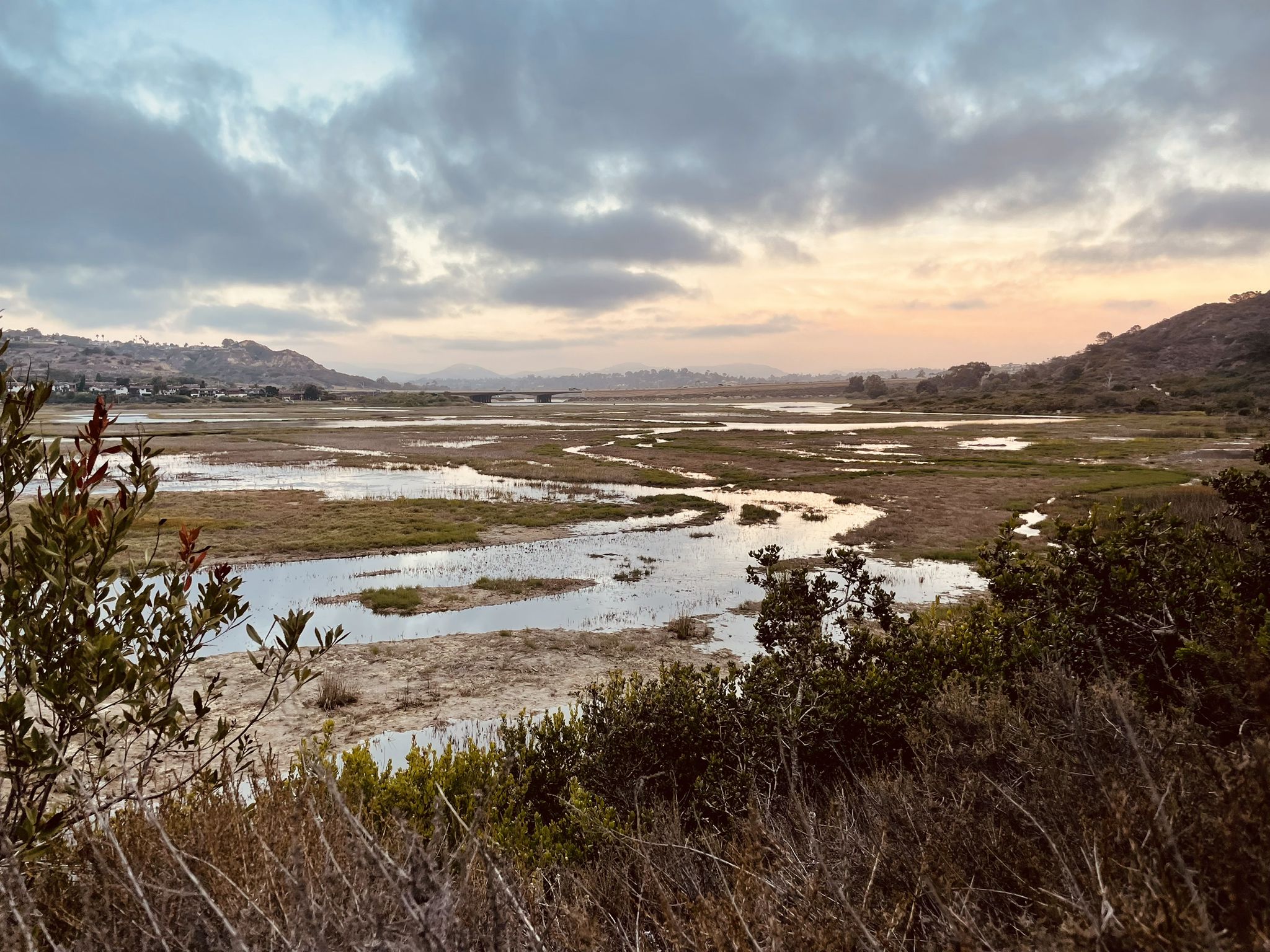 Wide view of a marshy estuary at sunset, with hills and clouds. - Pelican Island loop from Solana Beach