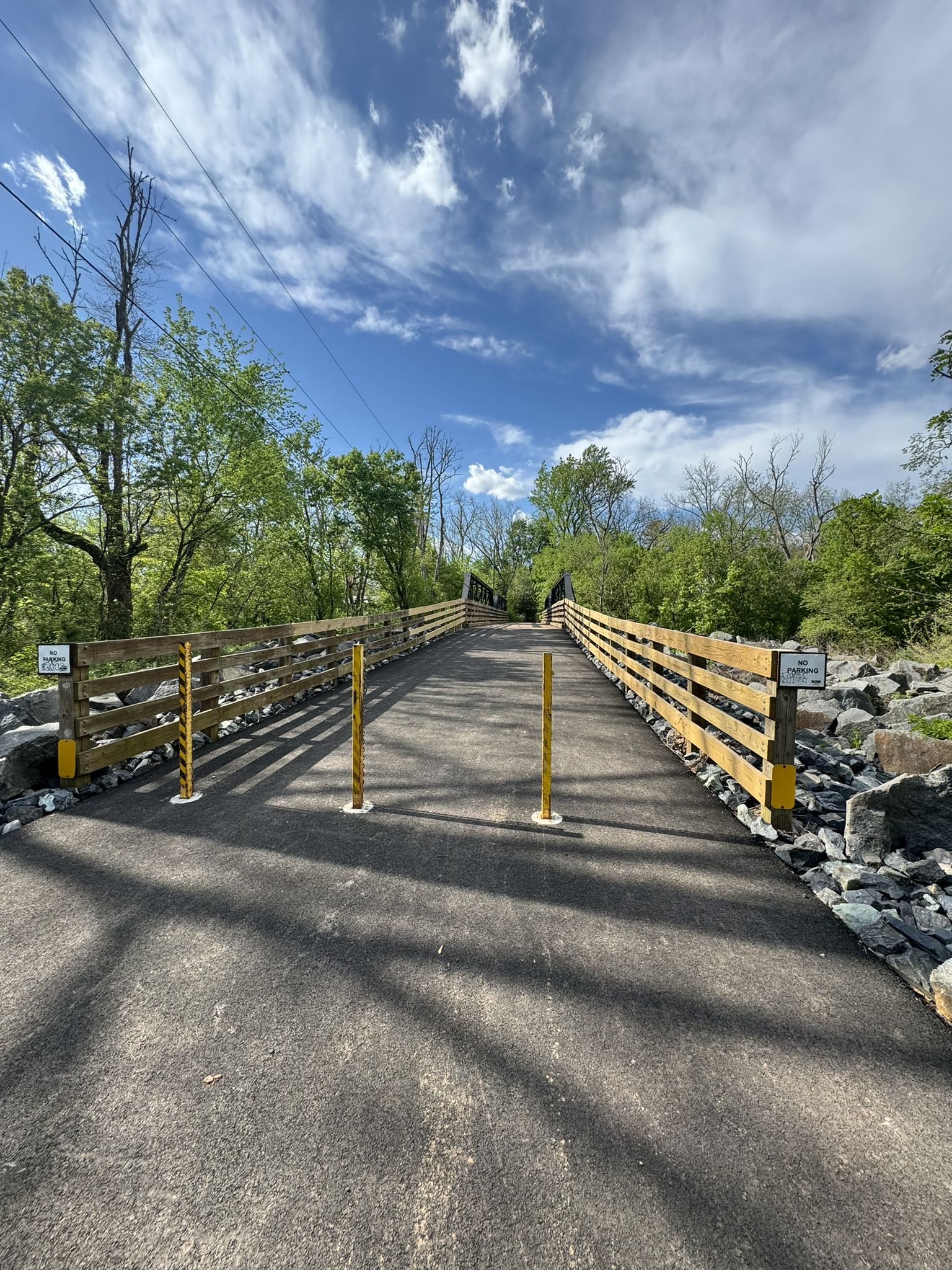 A paved trail with wooden fences and yellow posts under a bright blue sky. - Skippack Creek loop from Lansdale Septa