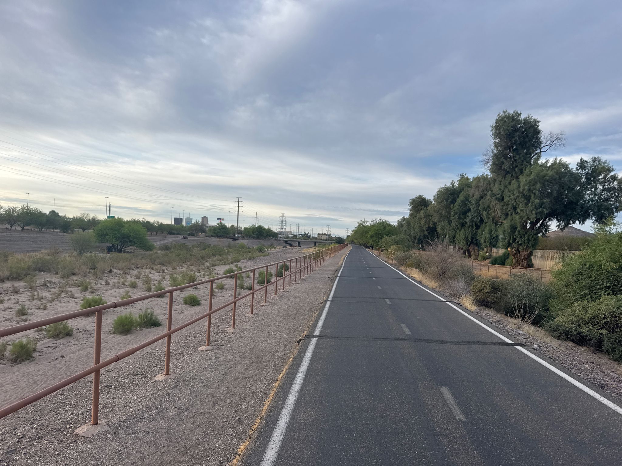 Paved path alongside a fence and dry brush, under a cloudy sky. - Mural by Joe Pagac – Presidio Inn loop from Tucson