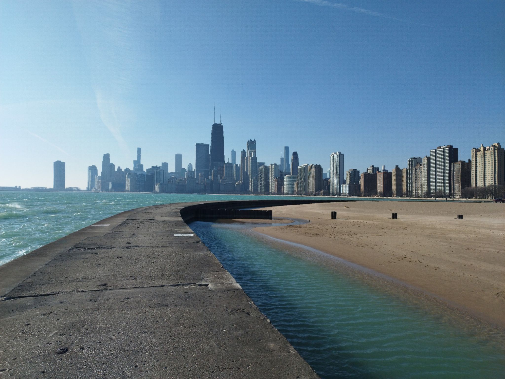 Concrete pier next to sandy beach and blue water, with city skyline. - Chicago Lakefront Trail