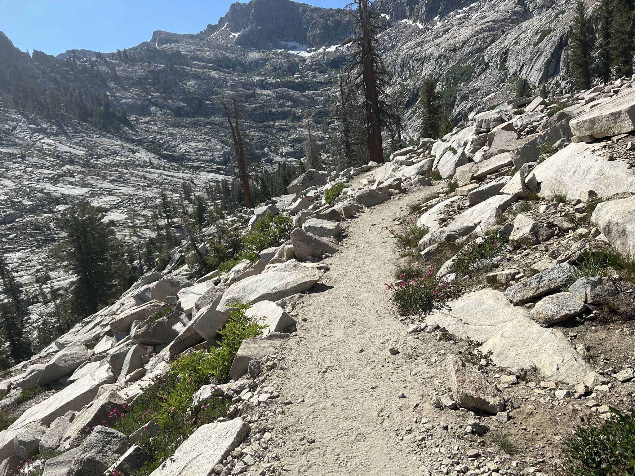 Dirt trail winding through rocky, mountainous terrain under bright sunlight. - Lakes Trail