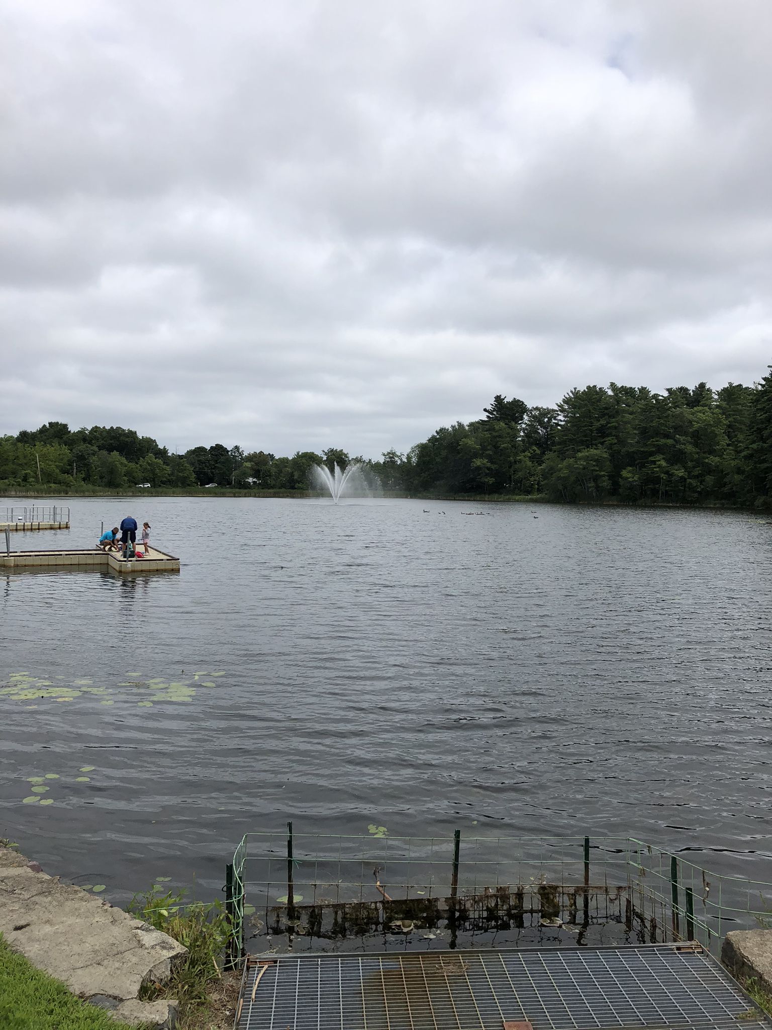 Overcast day at a lake with a fountain and people on a dock. - Independence Greenway Trail loop from Crystal Lake Conservation Area