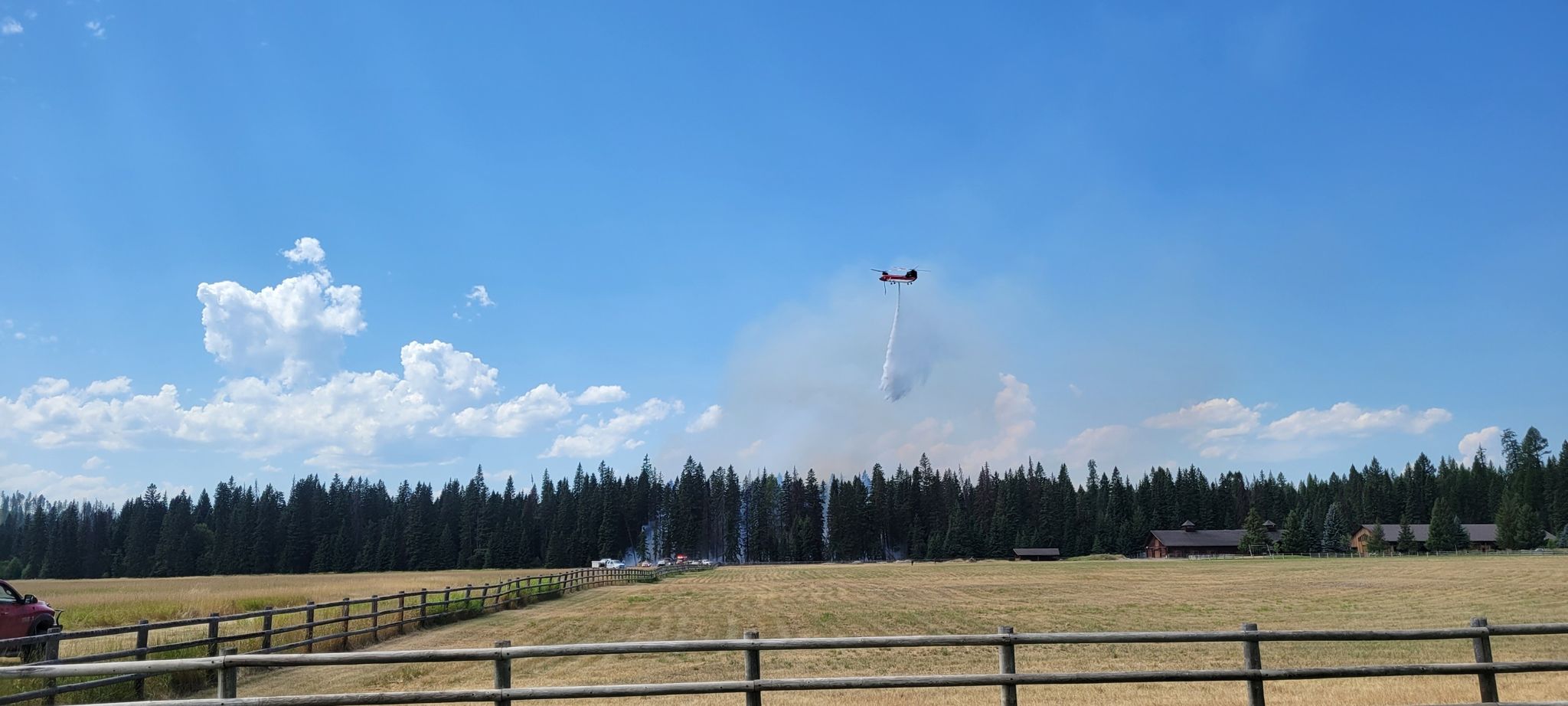 A firefighting plane drops water over a smoky forest on a sunny day. - Great Divide Mountain Bike Route