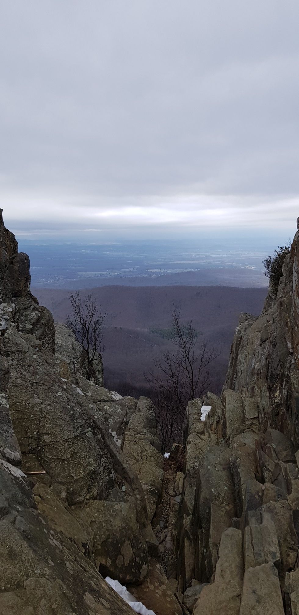 Rocky mountain vista framing a hazy, distant valley with snow patches. - Humpback Rocks Trail