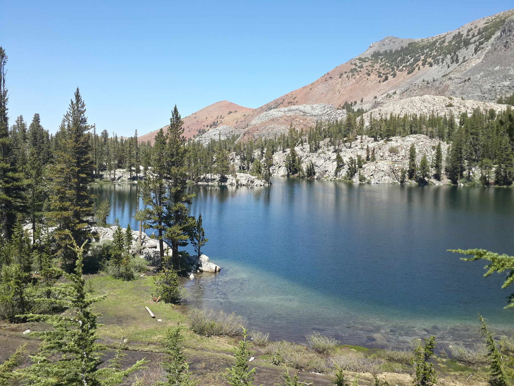 A serene lake with clear water, surrounded by green trees and mountains. - Duck Pass Trail