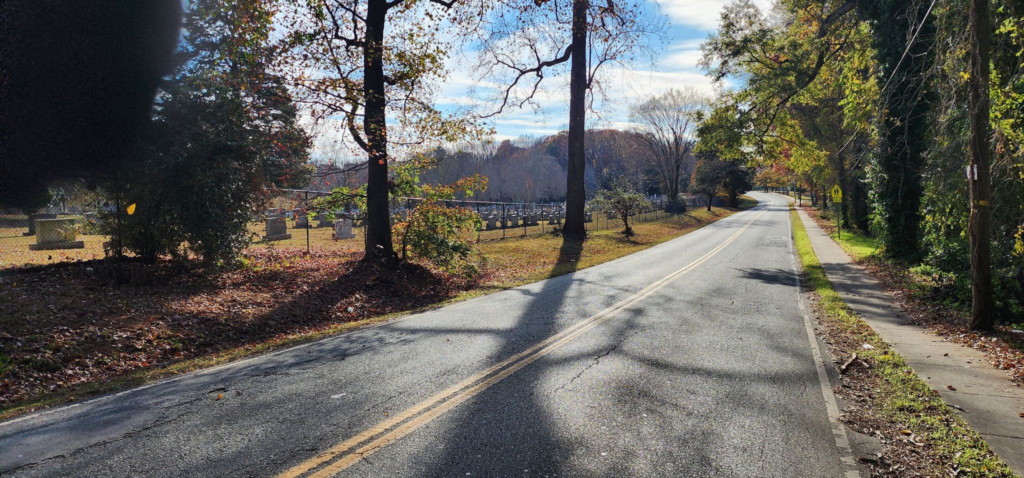Sunny road with autumn trees, long shadows, and a cemetery on the left. - Hiking loop from Kilborne Park