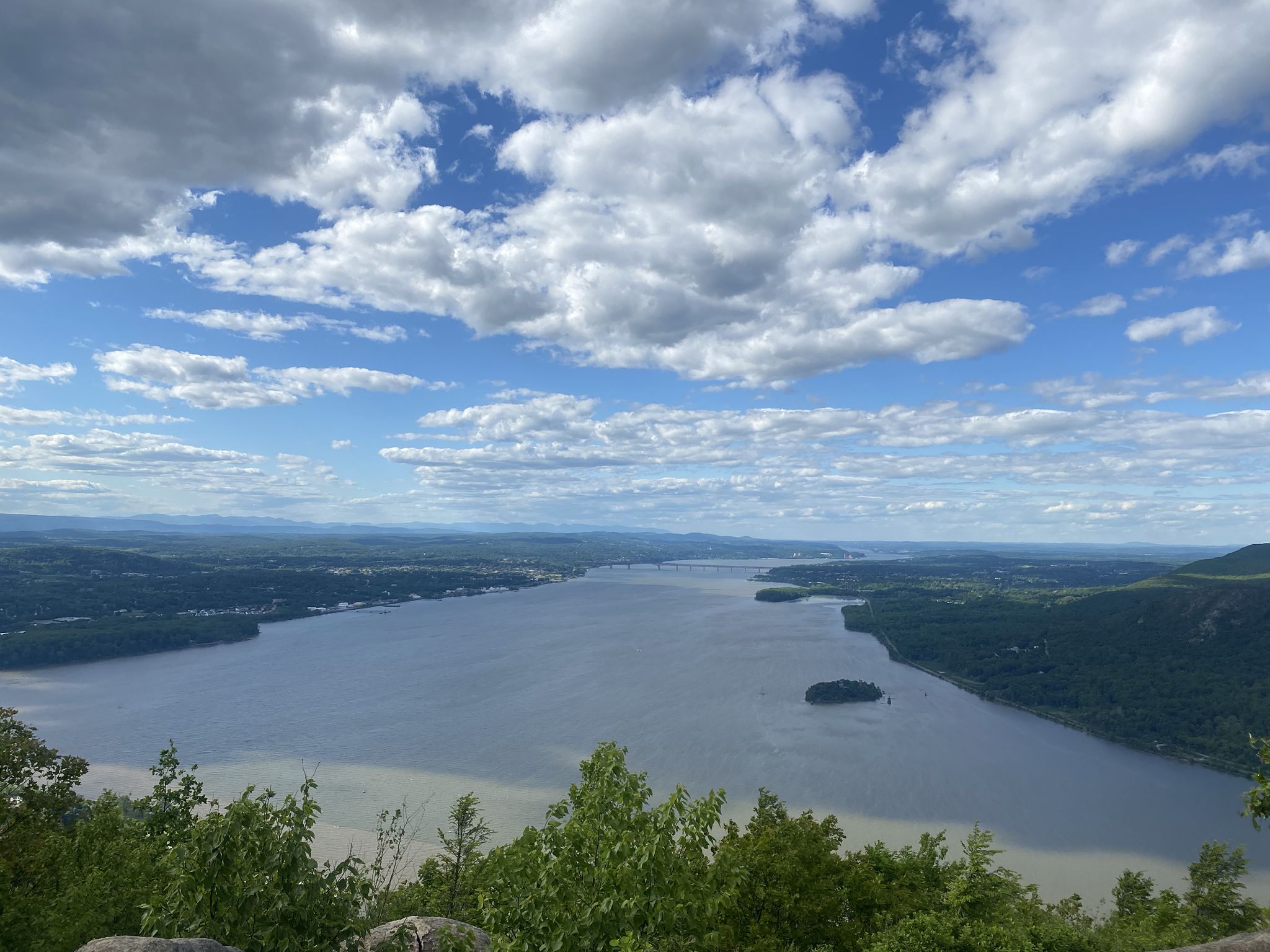 Panoramic view of a wide river winding through green forested hills under a cloudy sky. - Storm King Mountain via Bayview Avenue