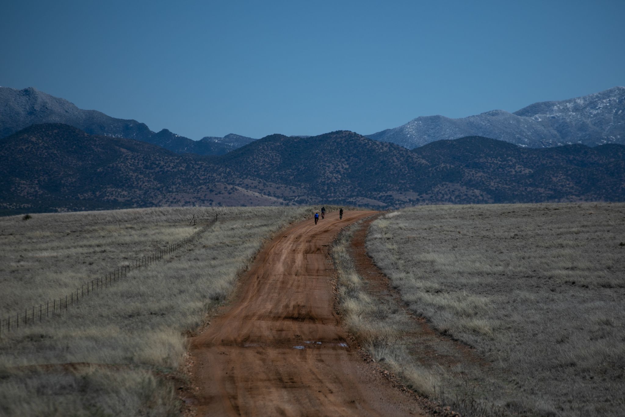 People walk on a long dirt road through grassy plains towards distant mountains. - Apache Road (Gravel) loop from Patagonia