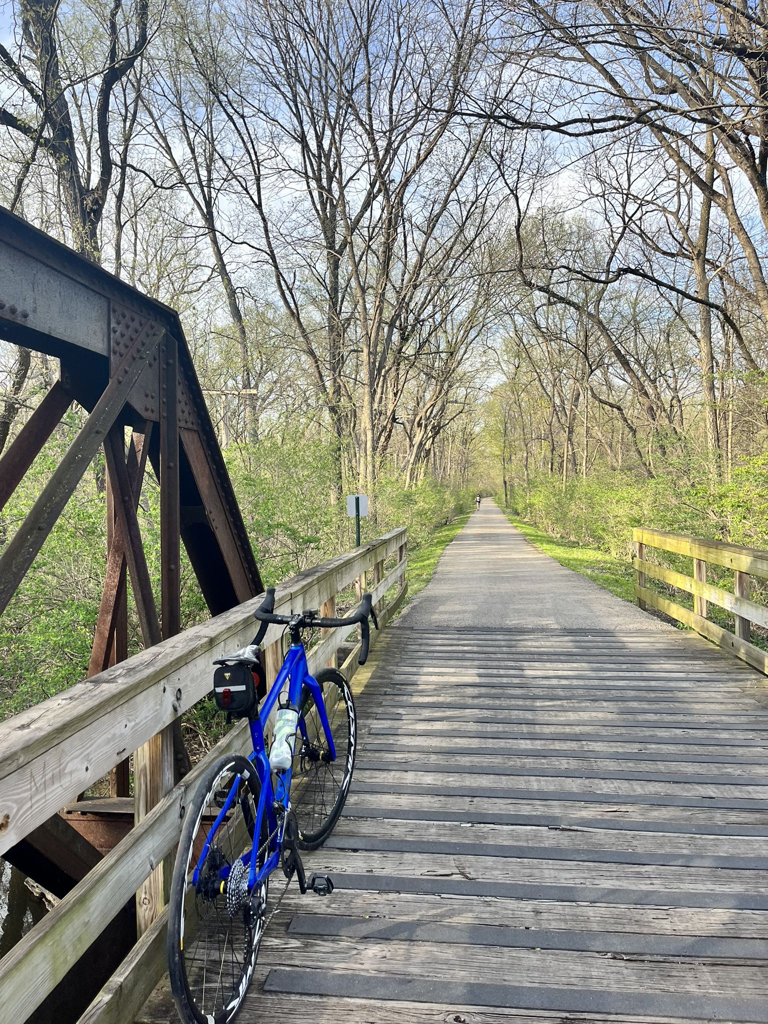 Blue bicycle leaning on a wooden bridge railing, leading to a tree-lined path. - Fox River Trail